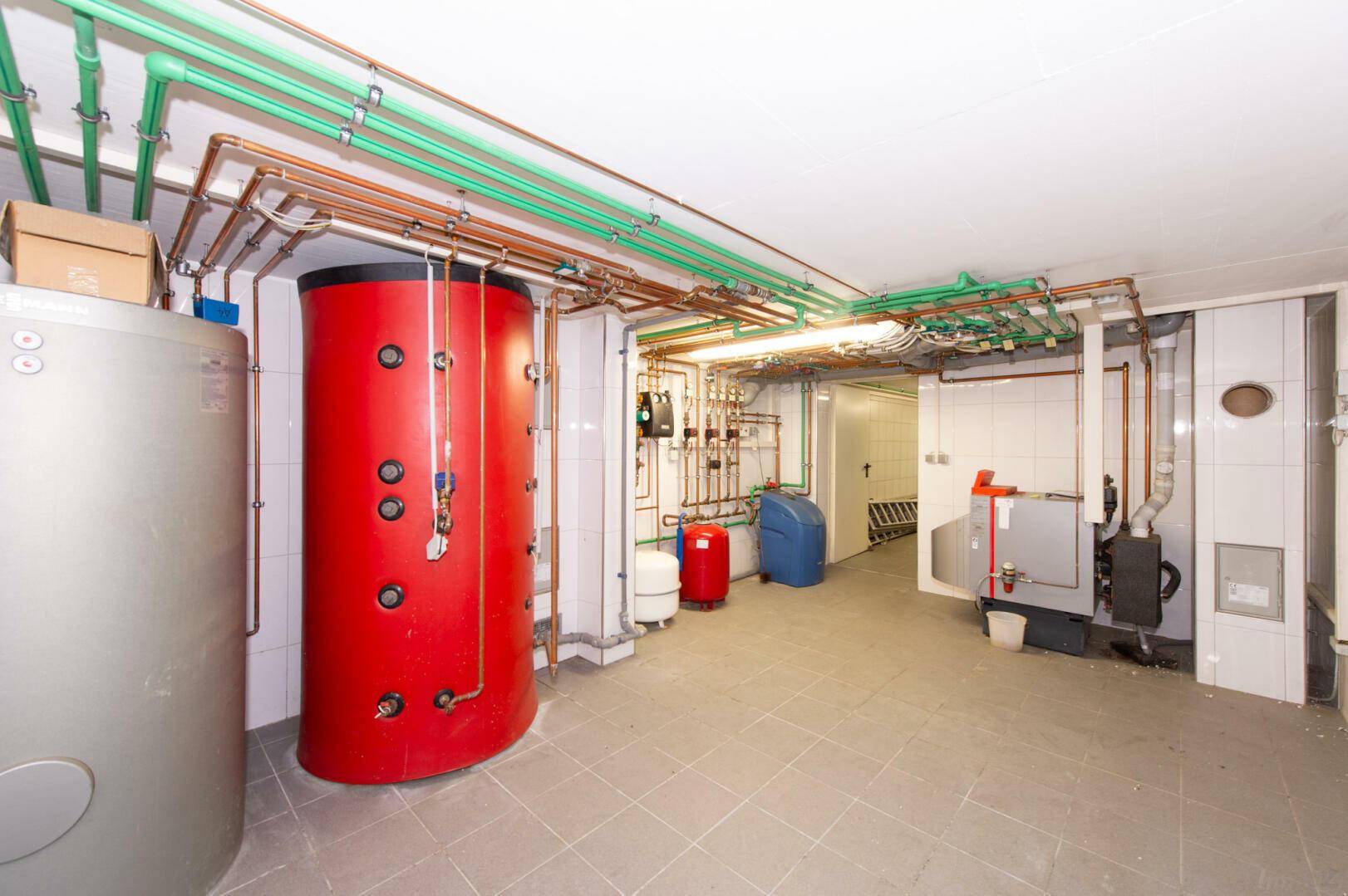 Technikraum im Keller mit Warmwasserspeichern und komplexen Rohrleitungen, funktional.