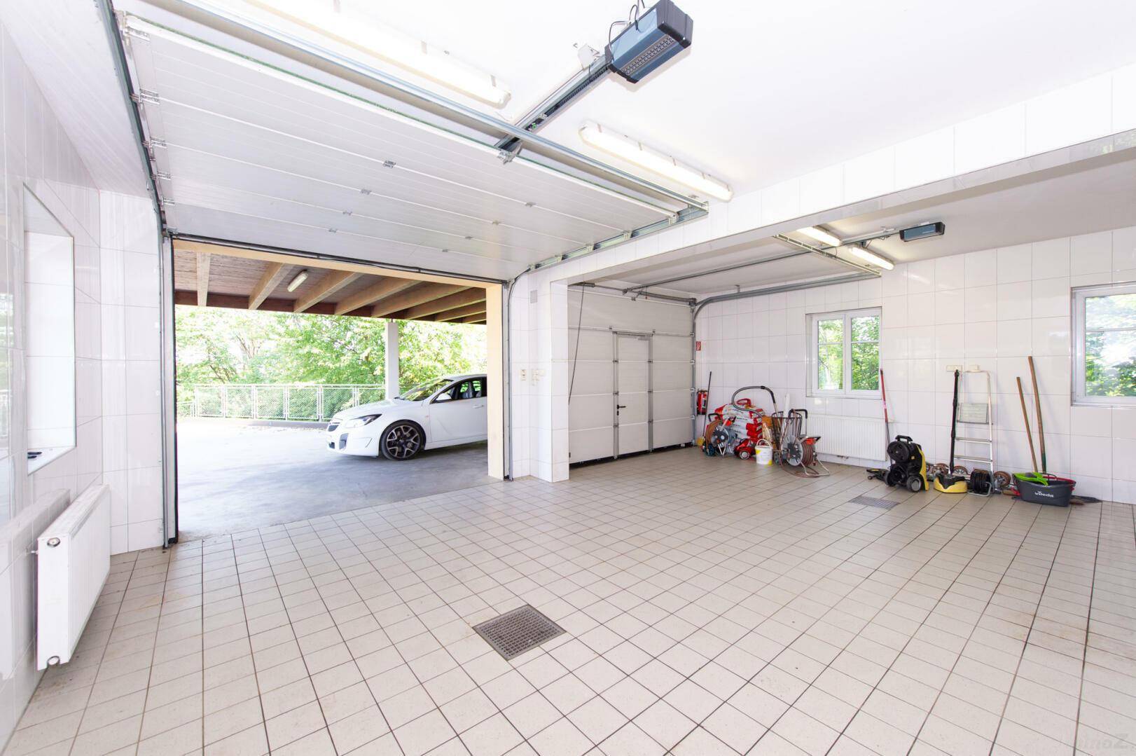 Helle Garage mit Fliesenboden und Zugang zum Carport, viel Stauraum und Arbeitsfläche.