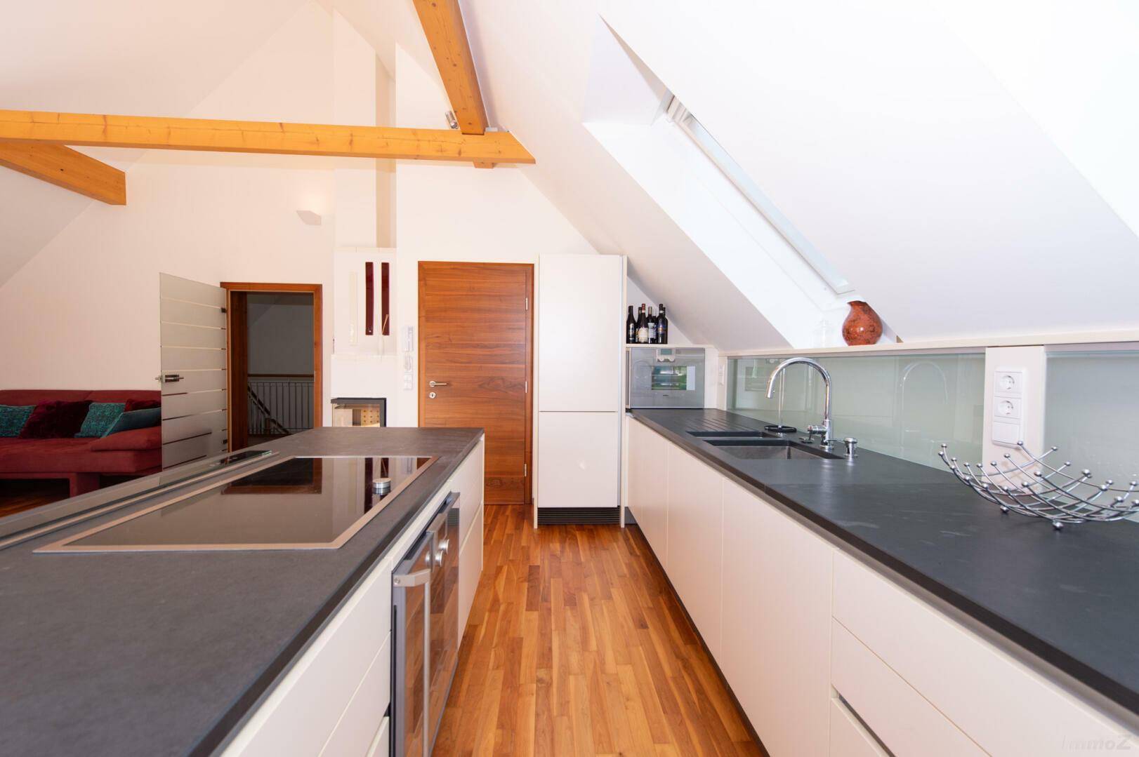 Moderne Küche im Dachgeschoss mit Kochinsel, dunkler Arbeitsplatte und Holzboden.