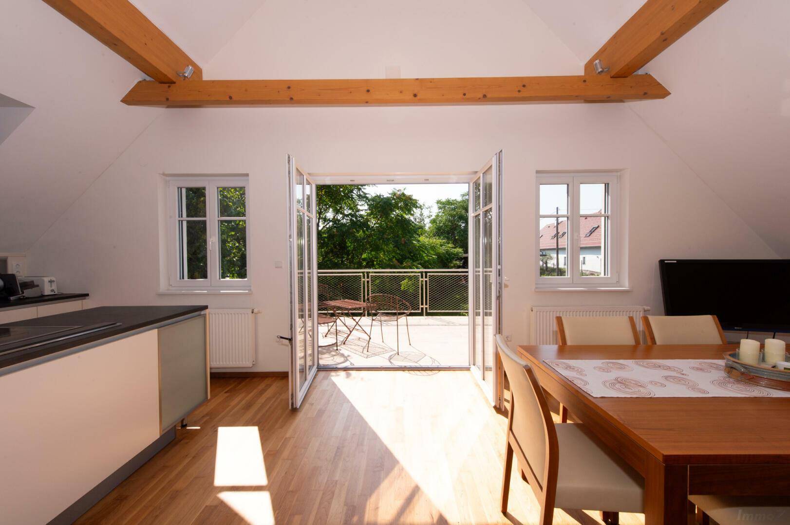 Heller Wohn-Essbereich im Dachgeschoss mit Zugang zum Balkon und Blick ins Grüne.