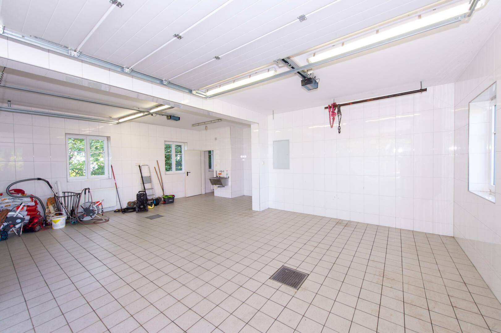 Große, geflieste Garage mit Rolltoren und Fenstern, ideal für mehrere Fahrzeuge oder Werkstatt.