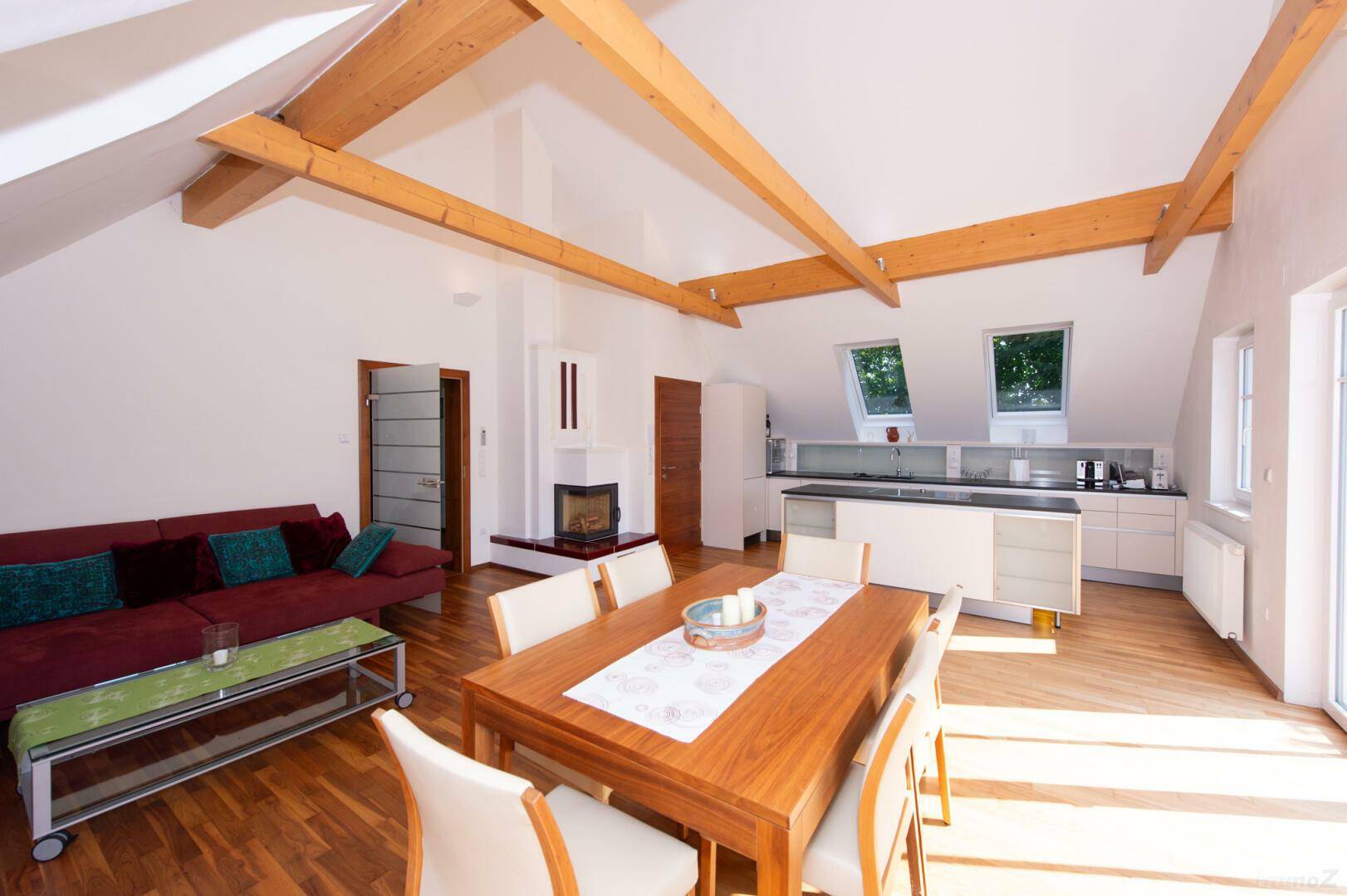 Gemütlicher Wohn-Essbereich im Dachgeschoss mit Kamin, Holzbalken und offener Küche.