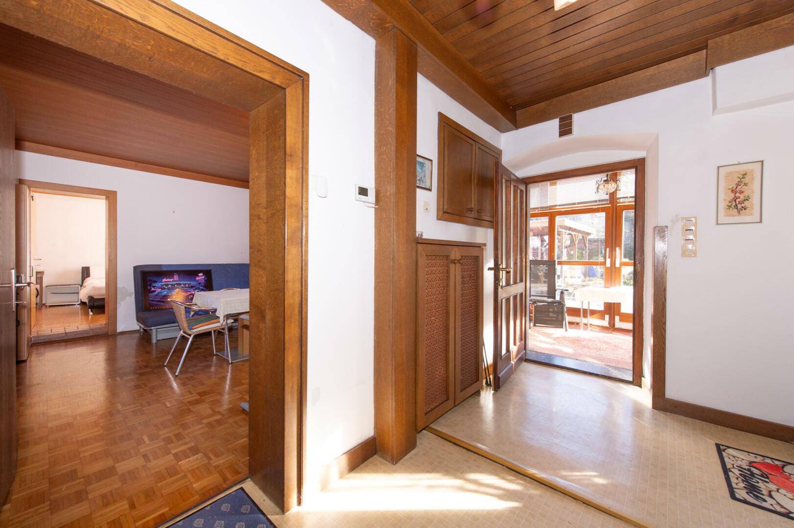 Eingangsbereich mit Holzvertäfelung, Parkettboden und Zugang zum Wintergarten.