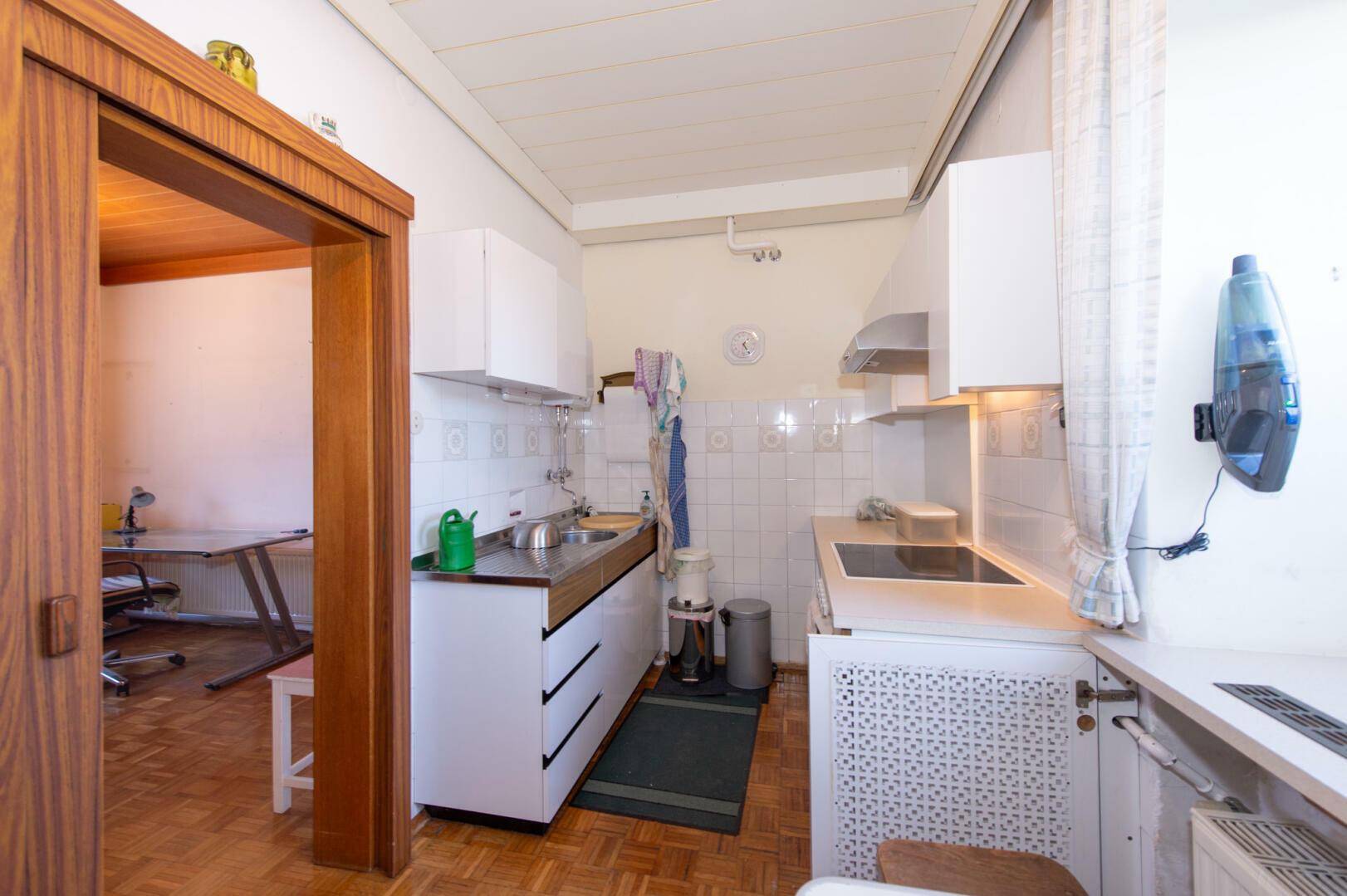 Kleine Küche mit weißen Schränken, Fliesenrückwand und Parkettboden.