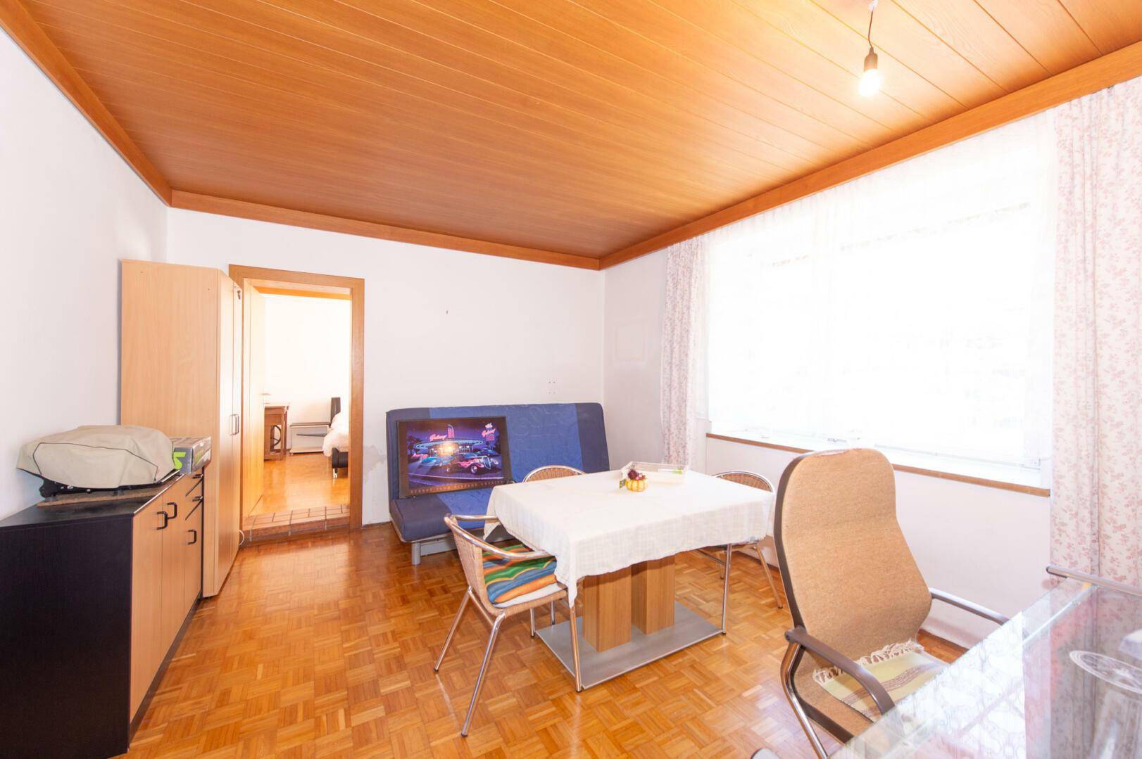 Helles Zimmer mit Parkettboden, Holzdecke und einem Esstisch.