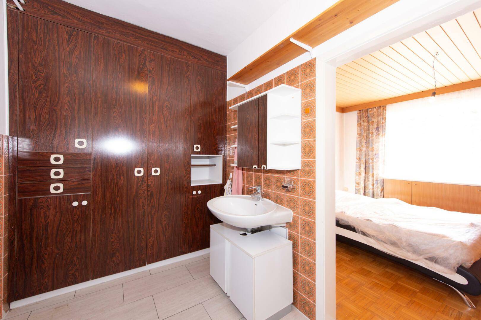 Badezimmer mit dunklen Holzschränken, Waschbecken und direktem Zugang zum Schlafzimmer.