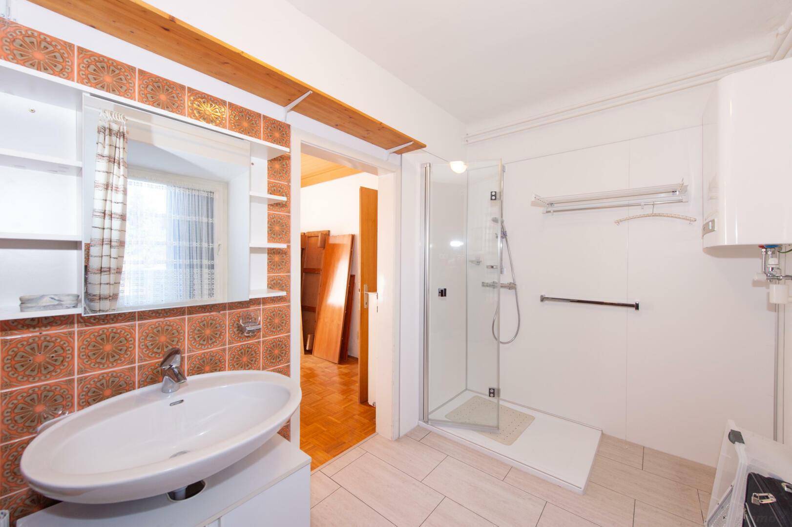 Badezimmer mit Dusche, Waschbecken und gemusterten Wandfliesen.