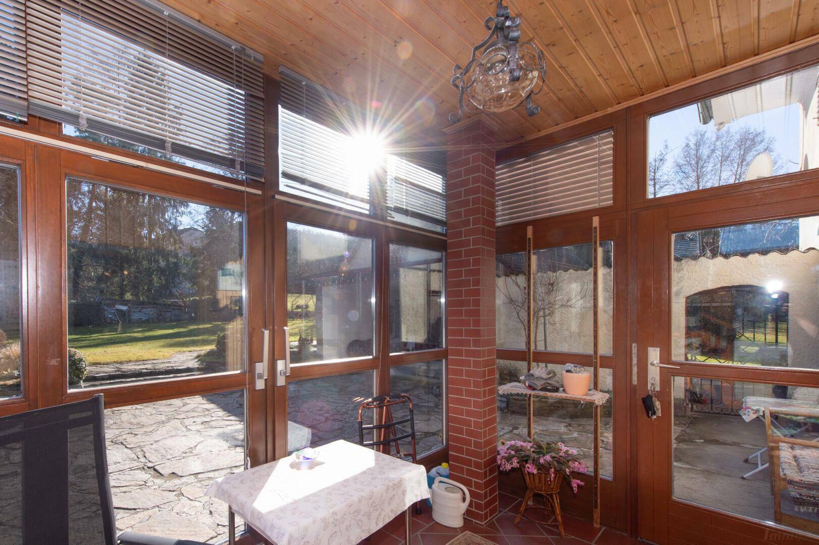Sonniger Wintergarten mit Holzdecke, Terrakotta-Fliesen und Blick in den Garten.