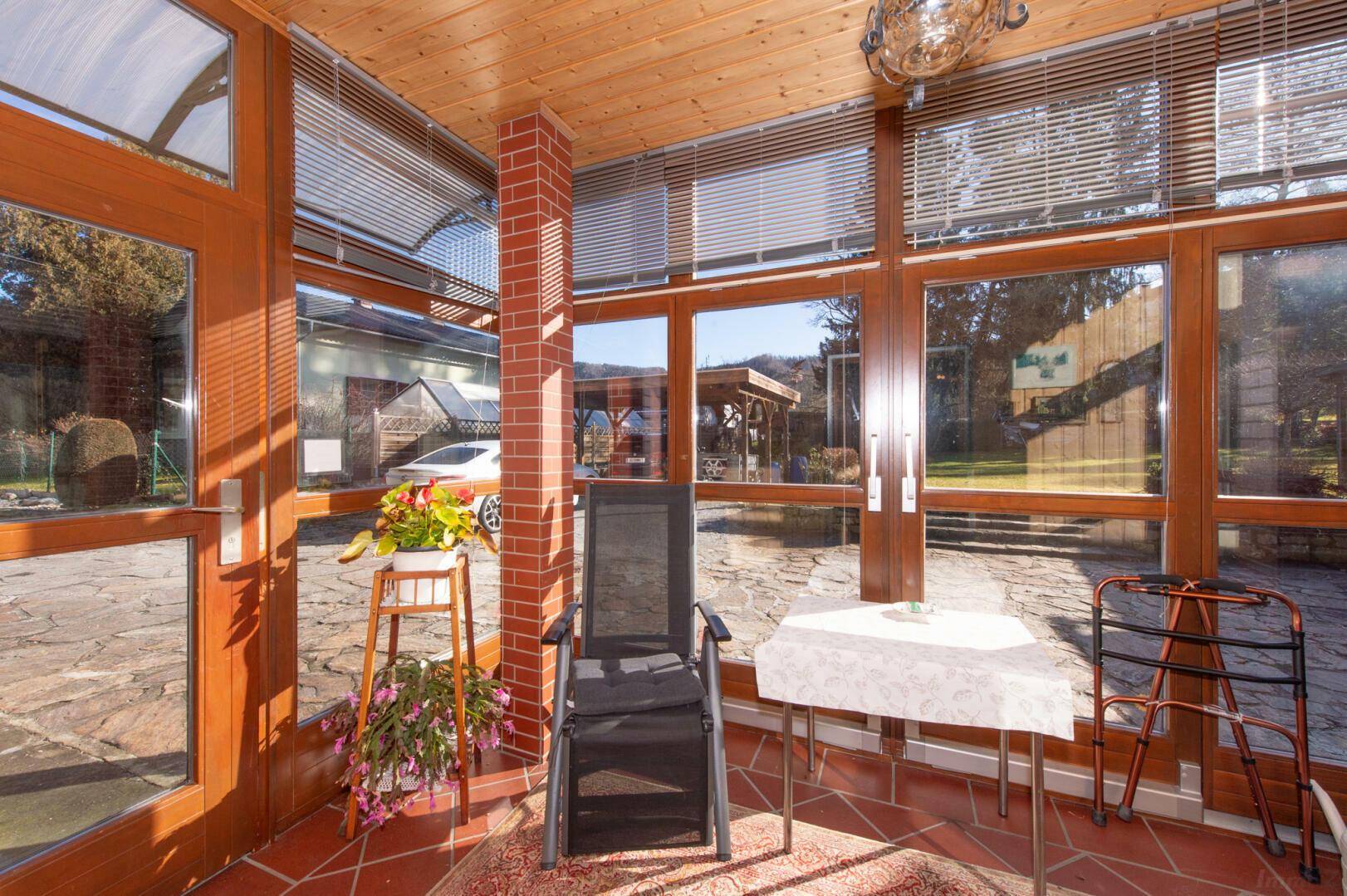 Heller Wintergarten mit großen Fenstern, Holzdecke und Terrakotta-Fliesenboden.