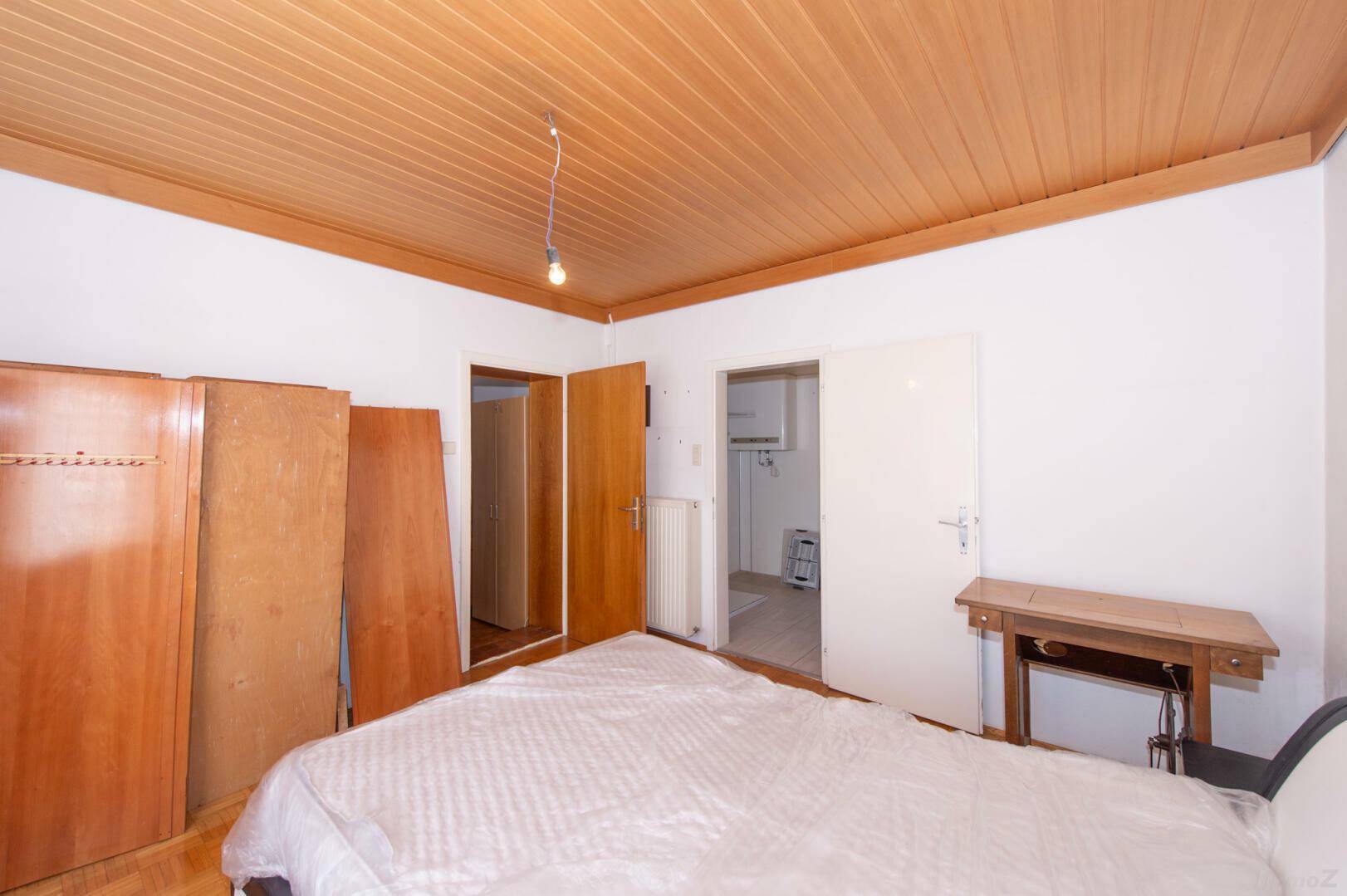 Schlafzimmer mit Holzdecke, Parkettboden und Zugang zu einem weiteren Raum.