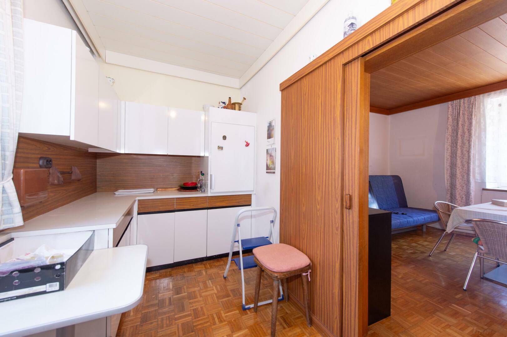 Kompakte Küche mit weißen Schränken, Parkettboden und Holzschiebetür.