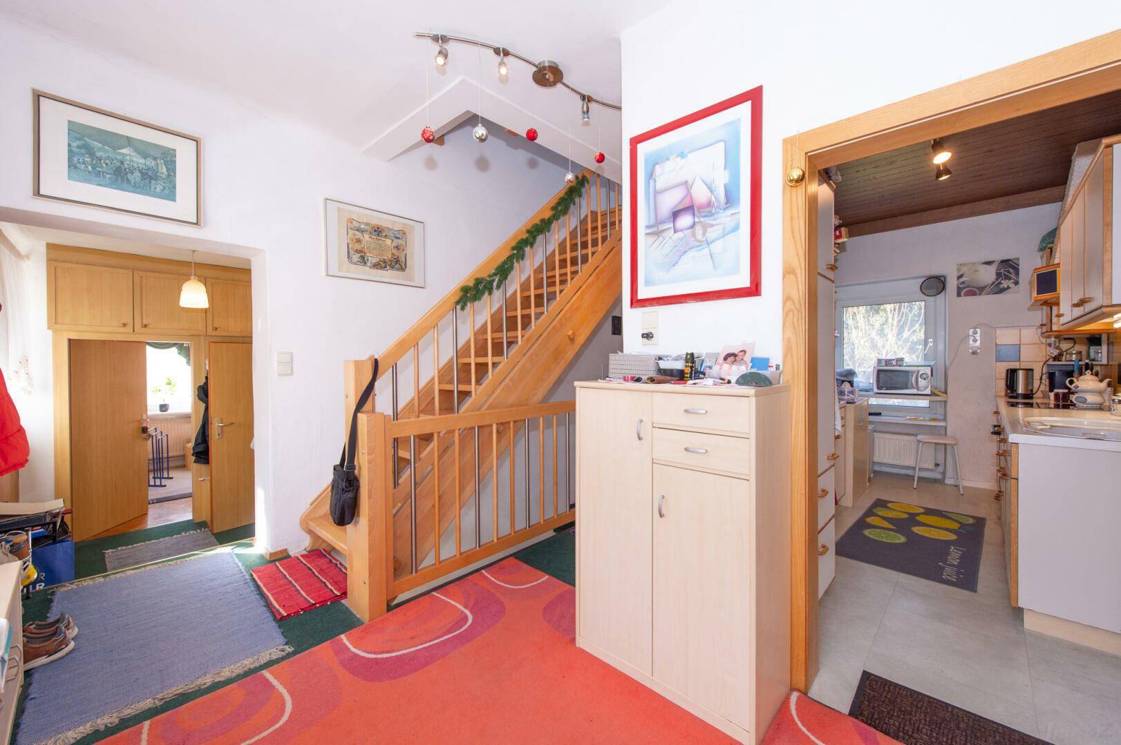 Flur mit Holztreppe, Garderobe und Zugang zur Küche.