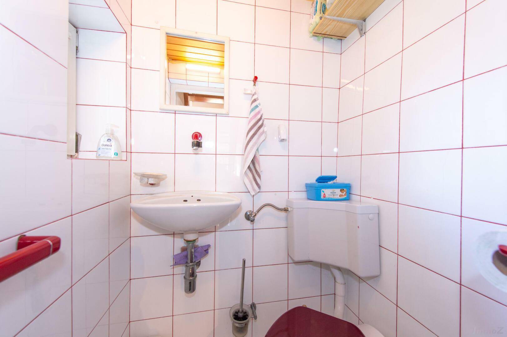Kleines Gäste-WC mit weißen Fliesen, Waschbecken und rotem Akzent.