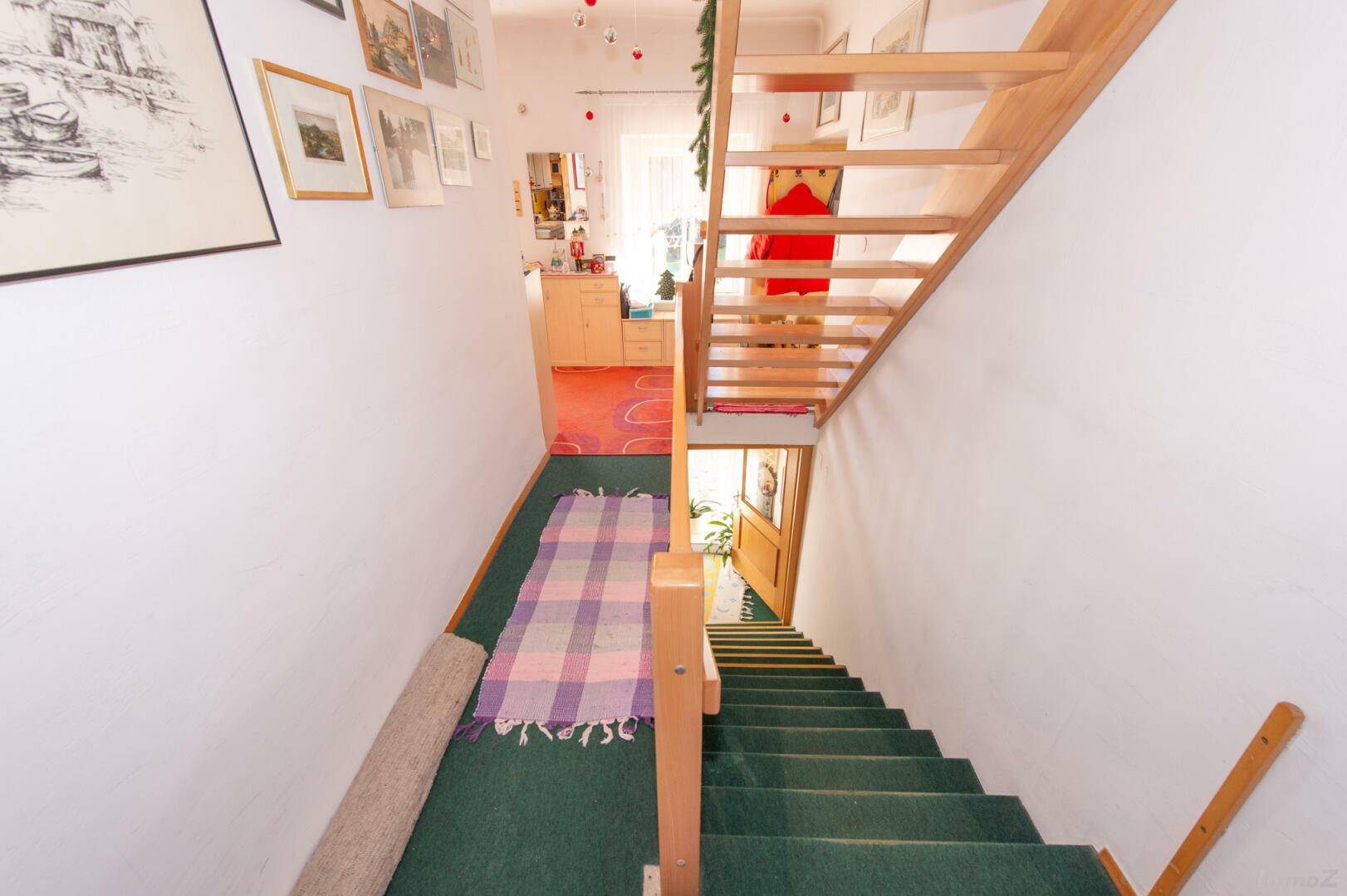 Treppenhaus mit grünem Teppichboden und hellem Holzgeländer.
