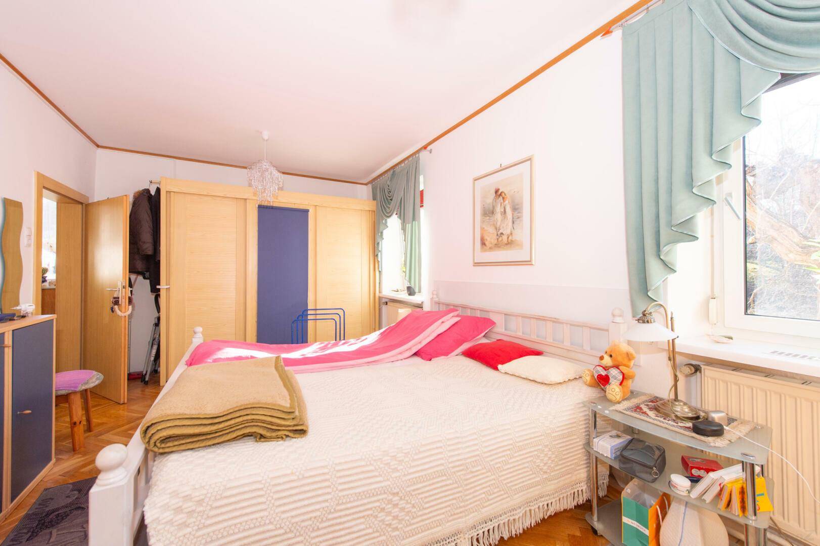 Helles Schlafzimmer mit Schiebetürenschrank, Parkettboden und Fenster.