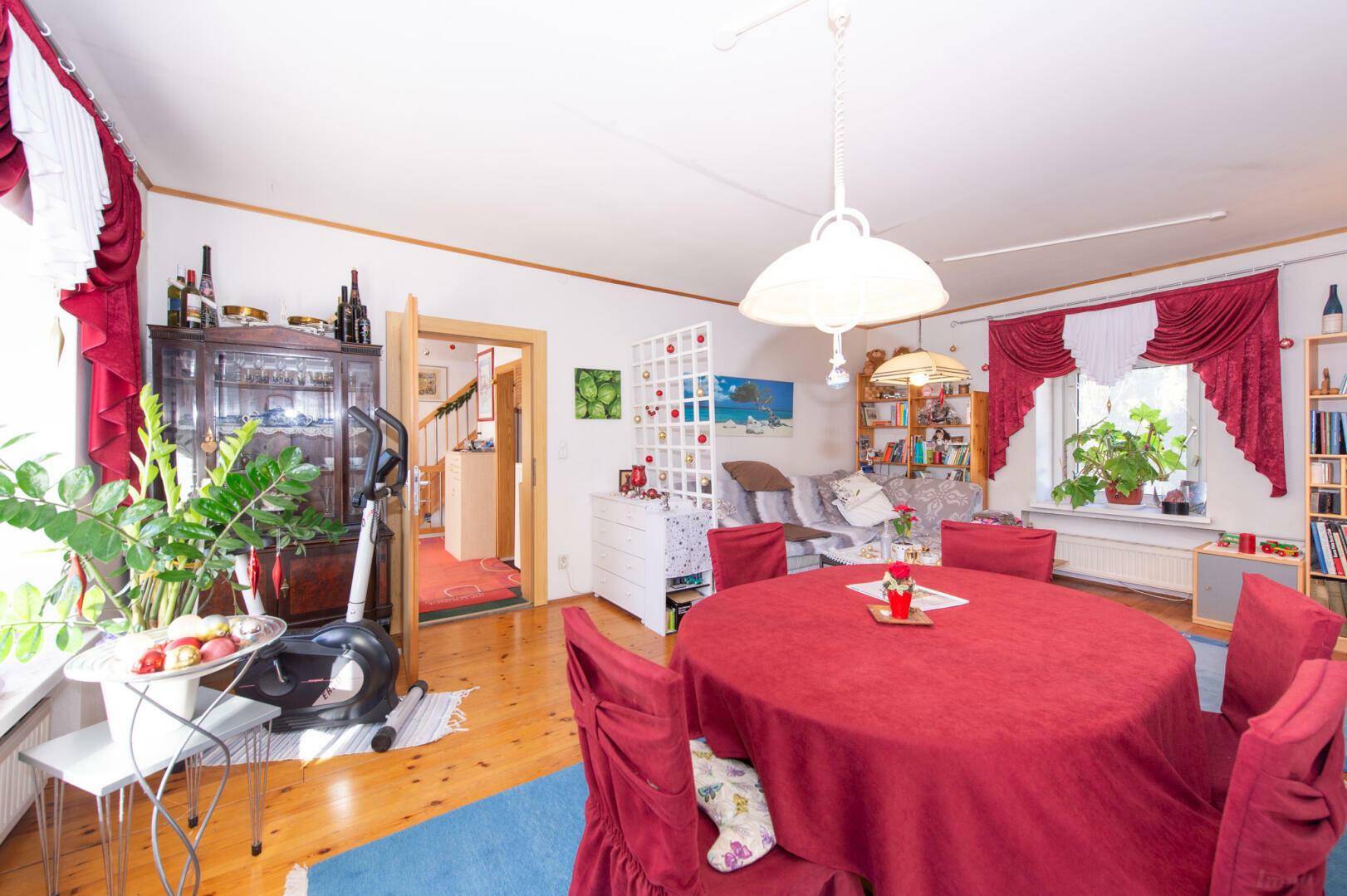 Wohn-Essbereich mit Holzboden, rotem Esstisch und blauer Teppichfläche.