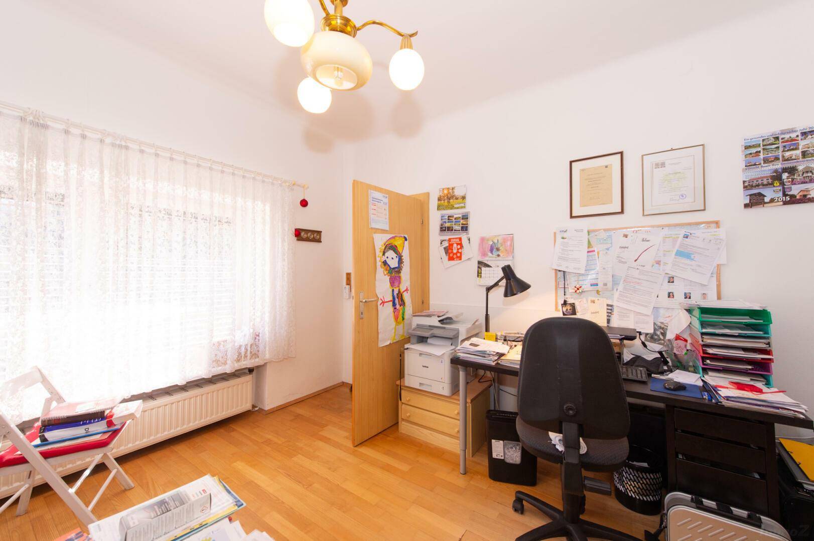 Helles Arbeitszimmer mit Schreibtisch, Drucker und Fenster.