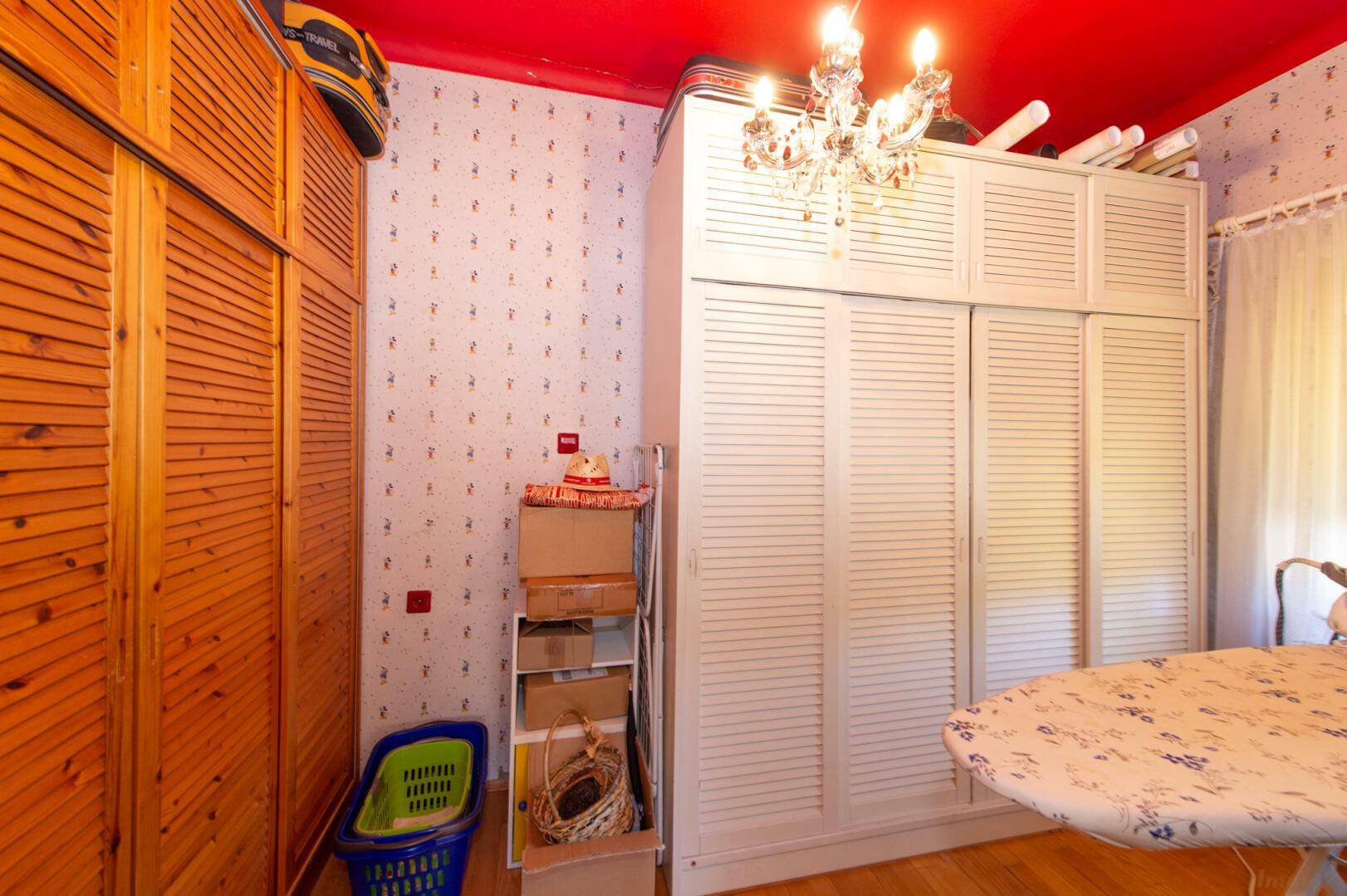 Abstellraum mit roten Decken, Schränken und Bügelbrett.