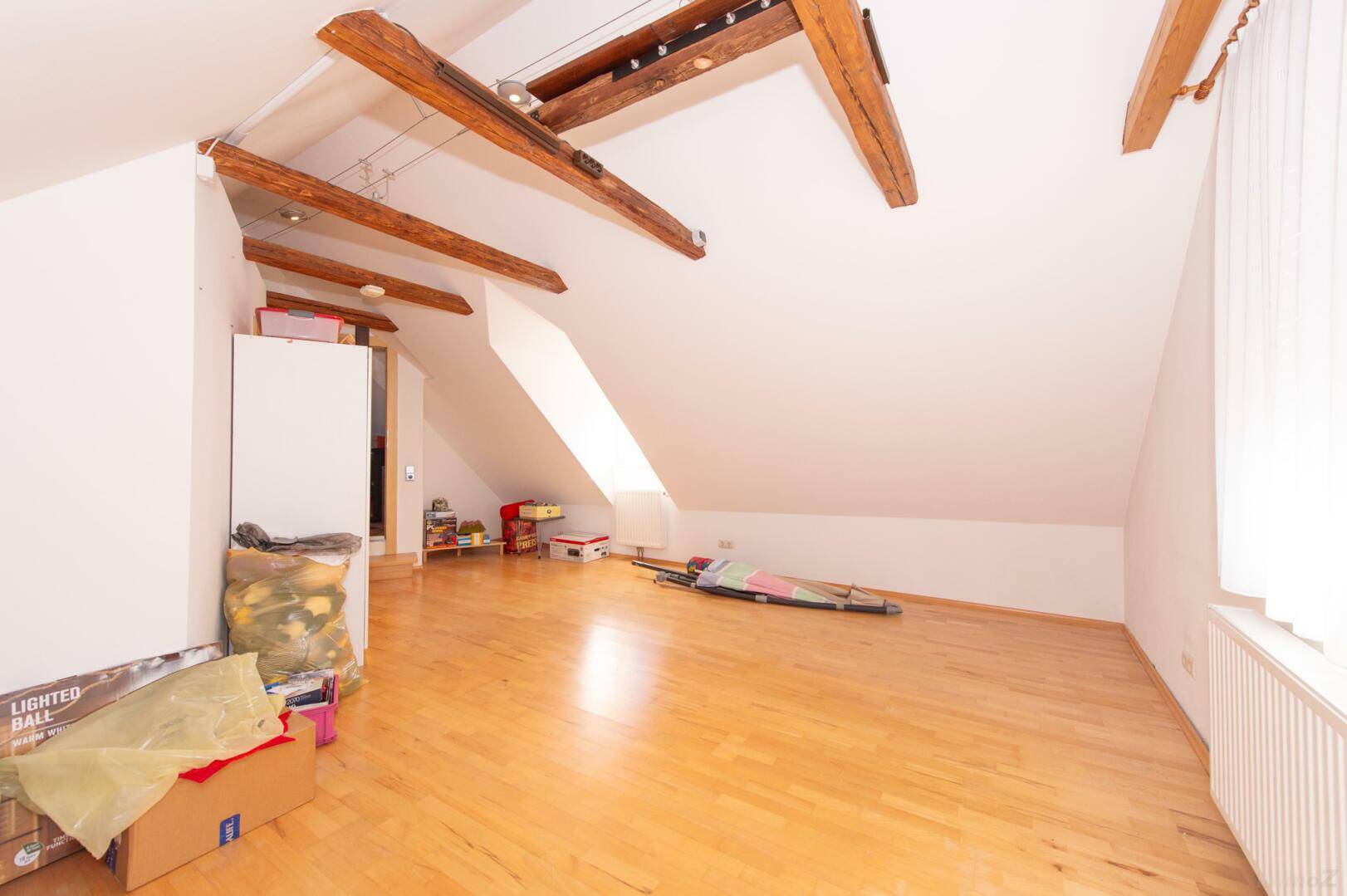 Geräumiger Dachboden mit Holzbalken, Holzboden und viel natürlichem Licht.