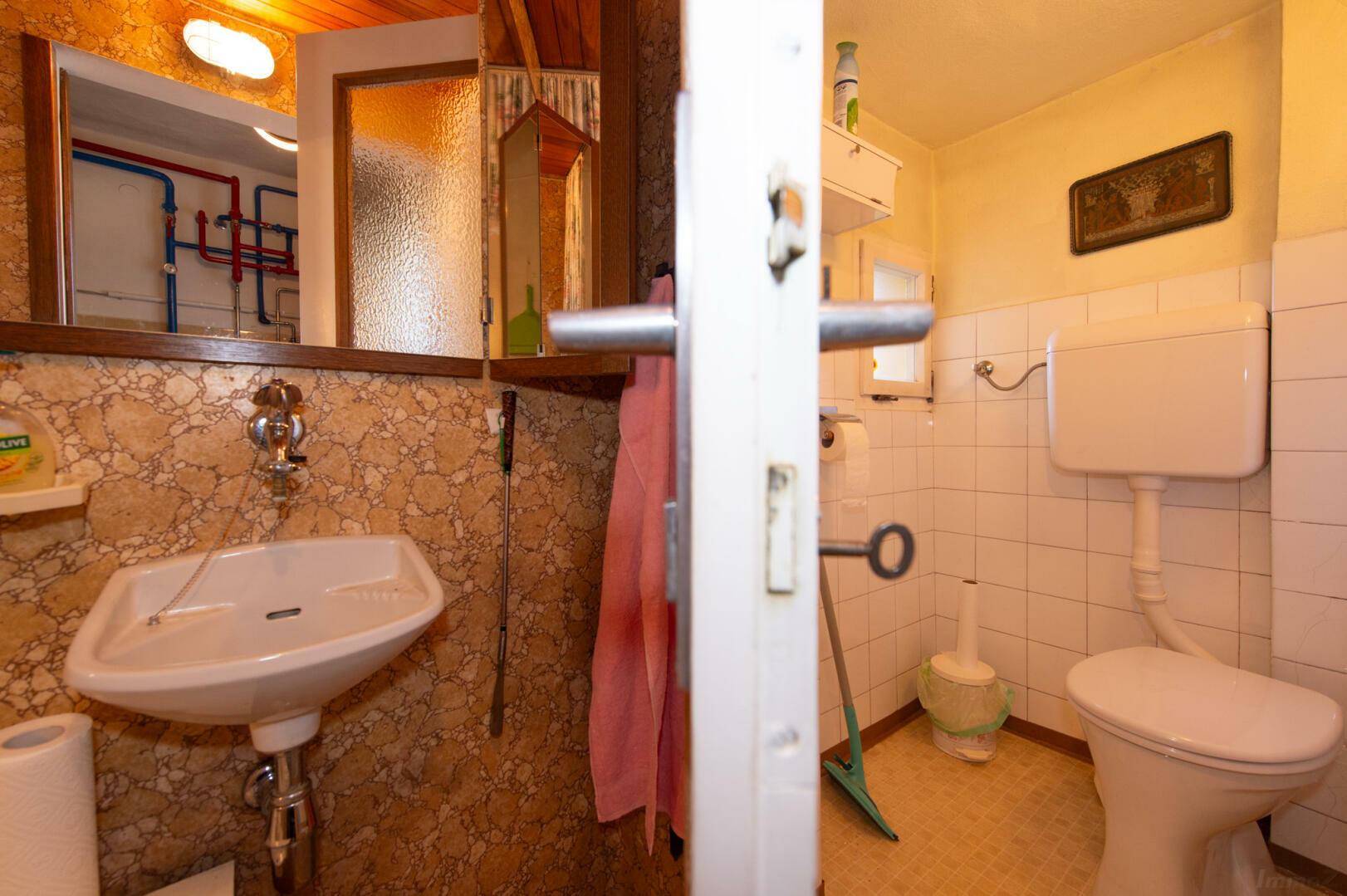 Kleines WC im Keller mit Waschbecken und Fliesen.