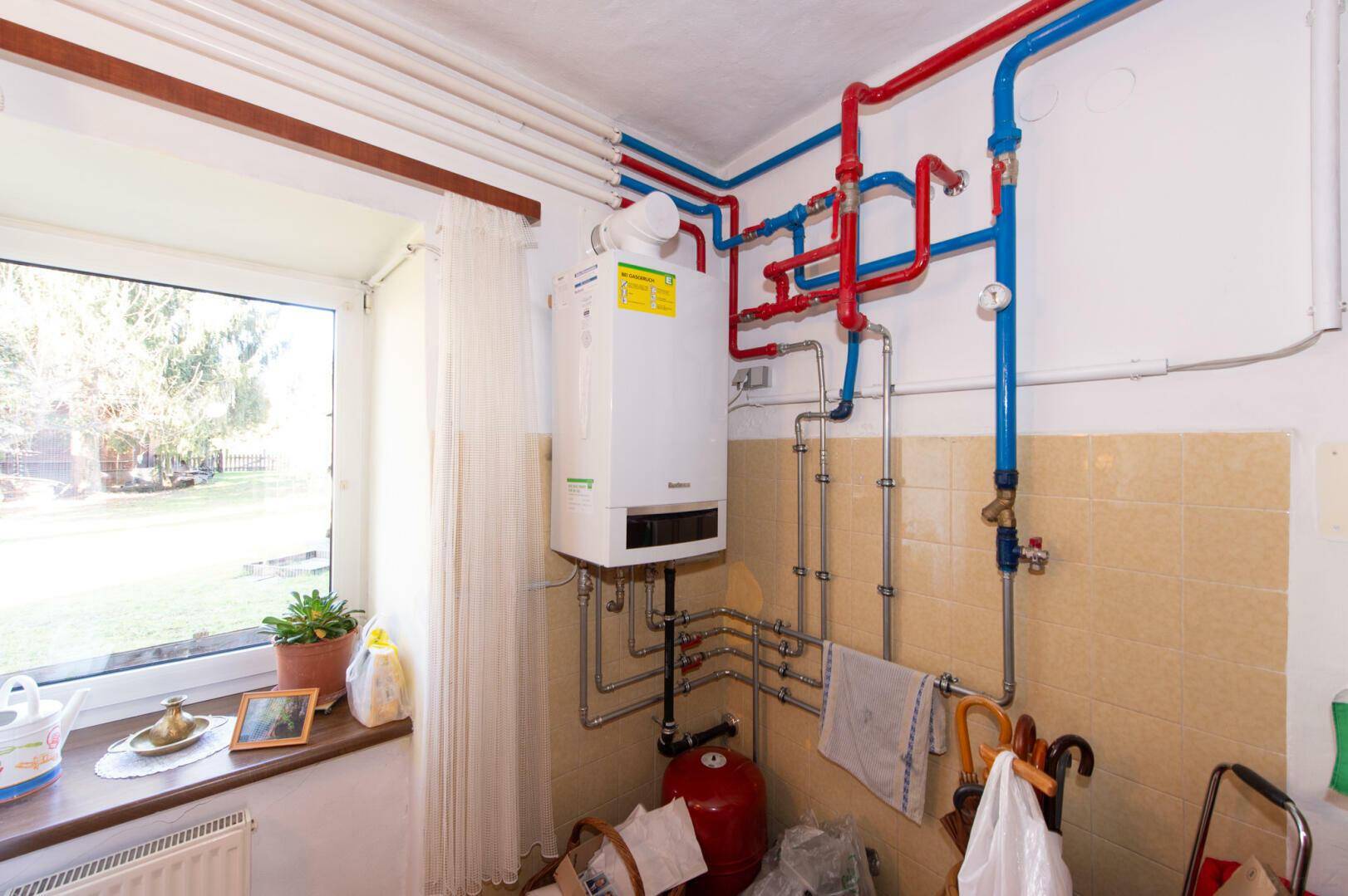 Heizungsraum mit Gastherme, sichtbaren Rohren und Fenster.