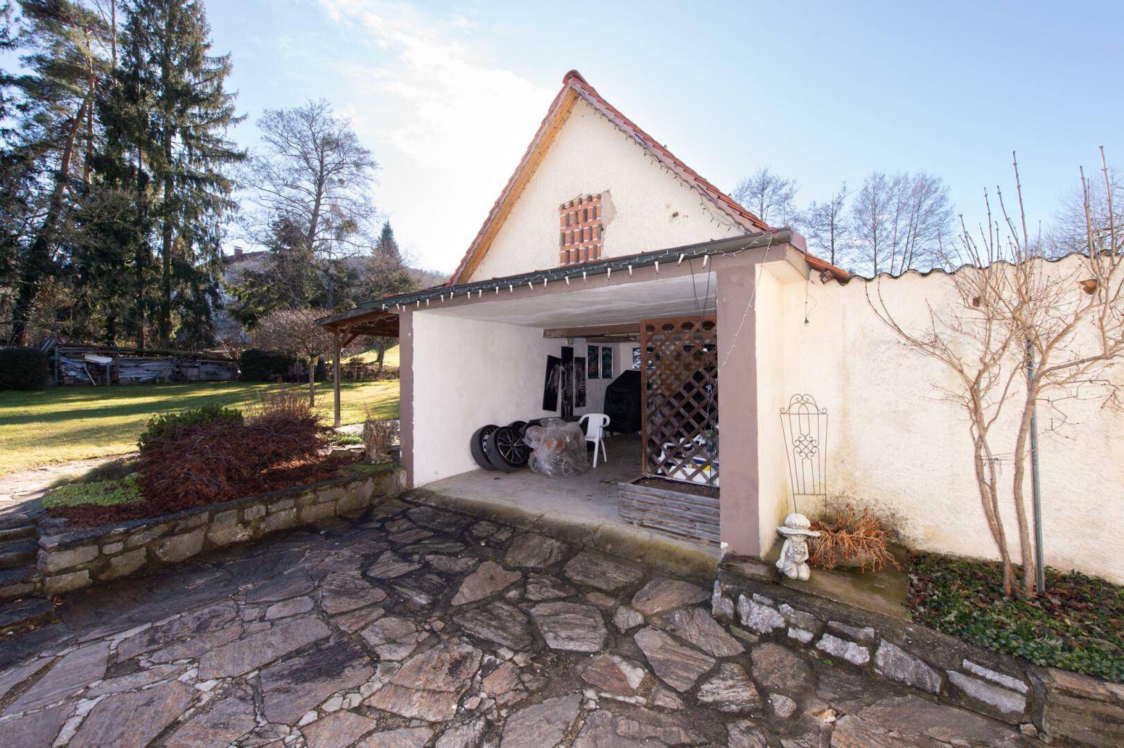 Carport und Garagenzufahrt mit Steinpflaster und Gartenbereich.