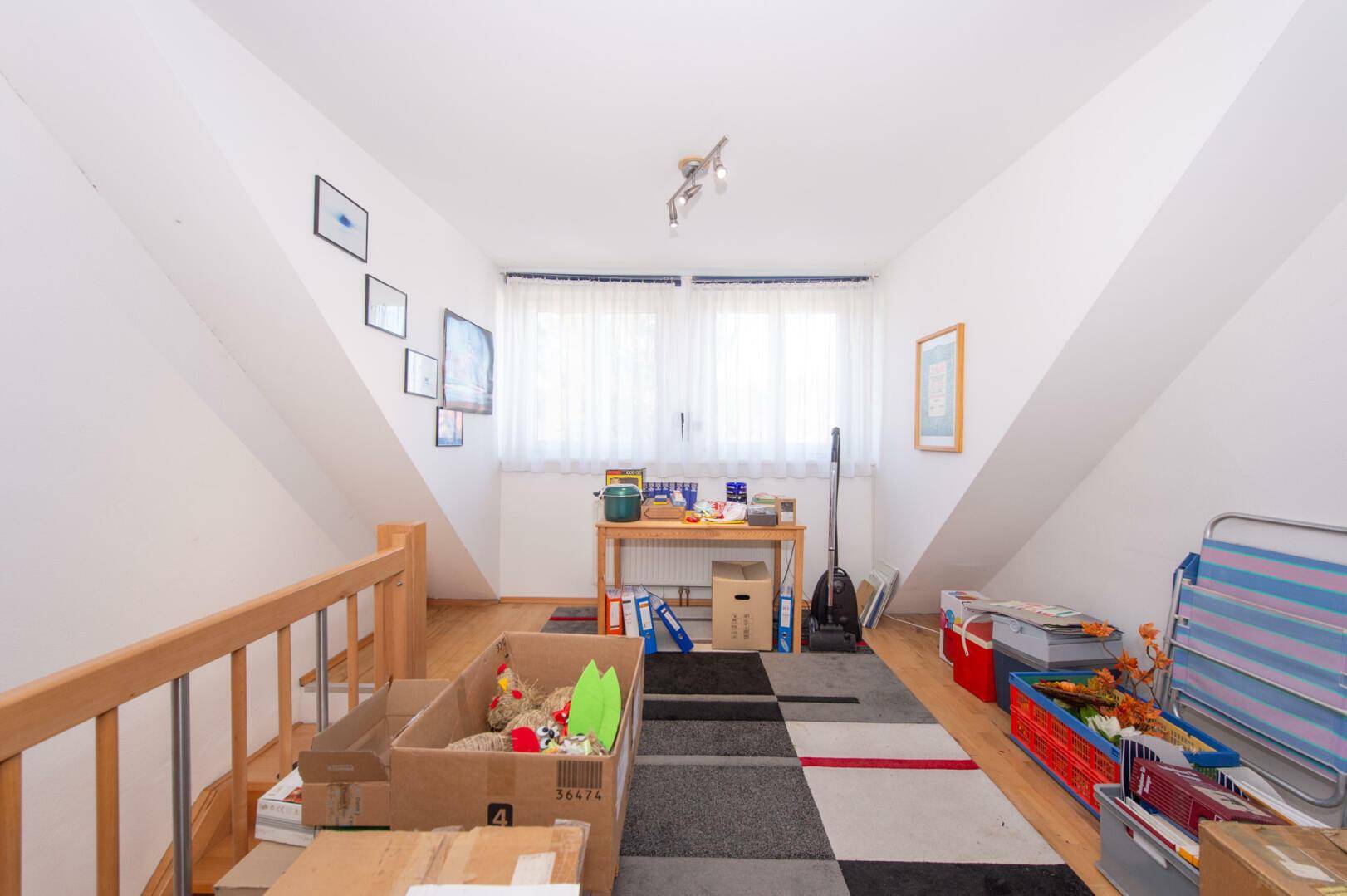 Ausgebauter Dachbodenbereich mit Schrägen, Holzboden und Fenster.