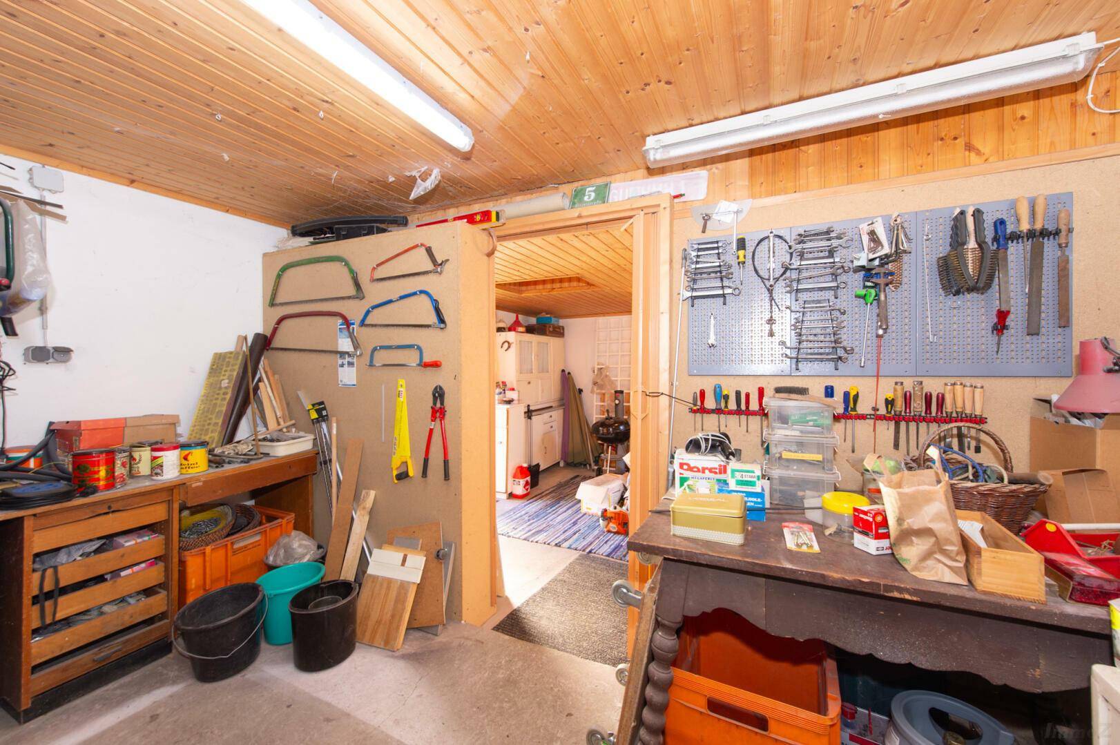 Werkstatt mit Werkzeugwänden und Zugang zu einem weiteren Raum.