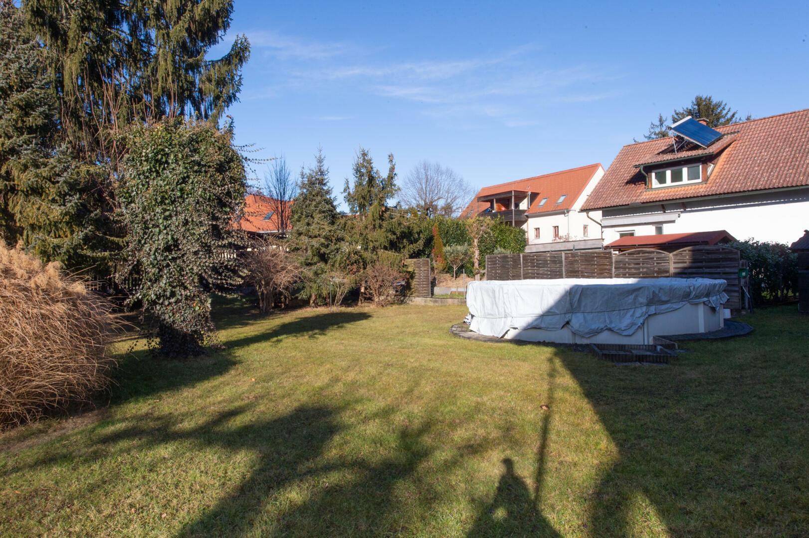 Großer Garten mit Rasenfläche, Bäumen und einem Aufstellpool.