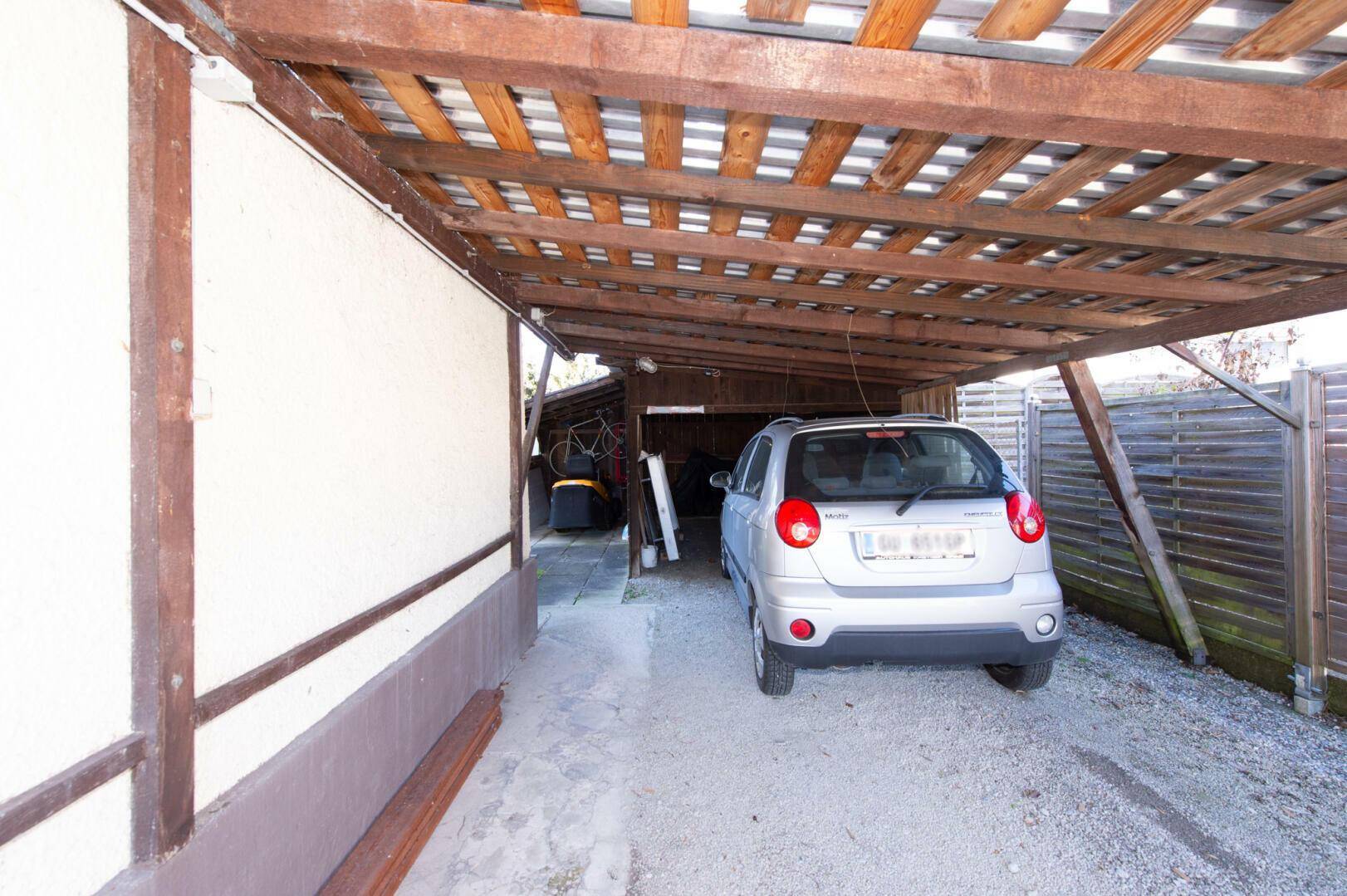 Überdachter Carport mit Holzbalken und Parkfläche für ein Fahrzeug.