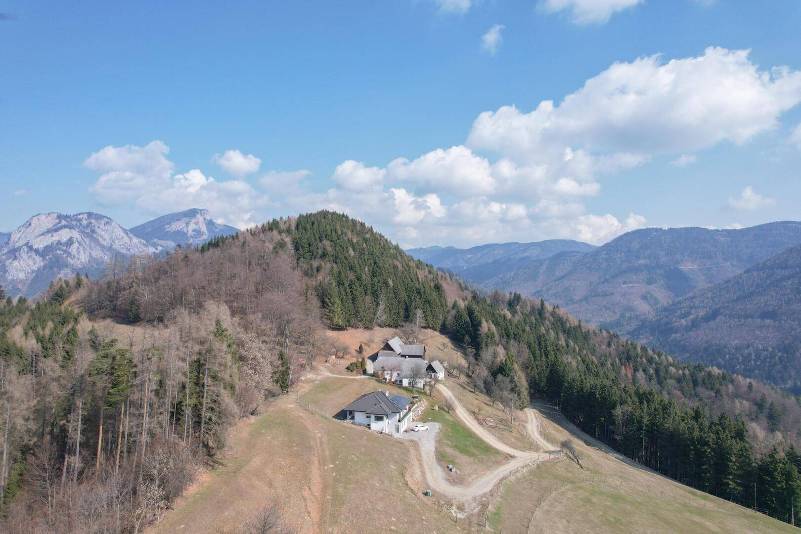Weitläufige Luftaufnahme der Anwesen in einer malerischen Berglandschaft unter blauem Himmel.