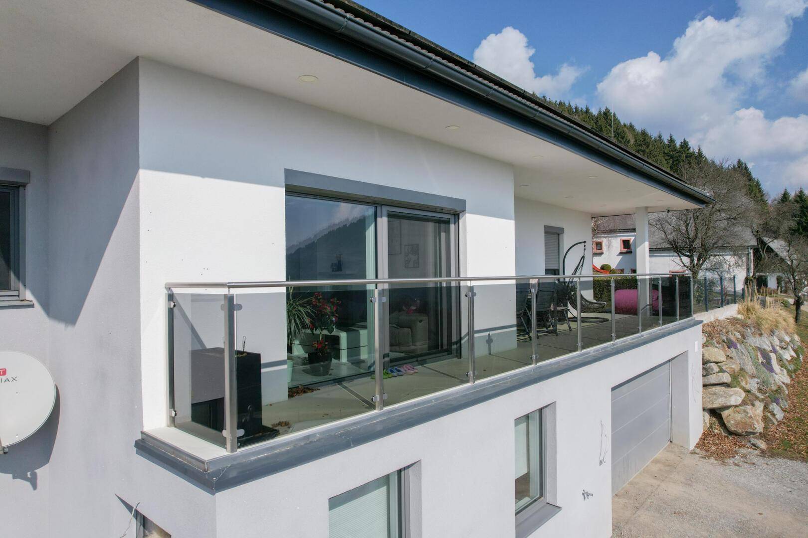 Moderne Hausfassade mit großem Balkon und Glasgeländer in sonniger Lage.