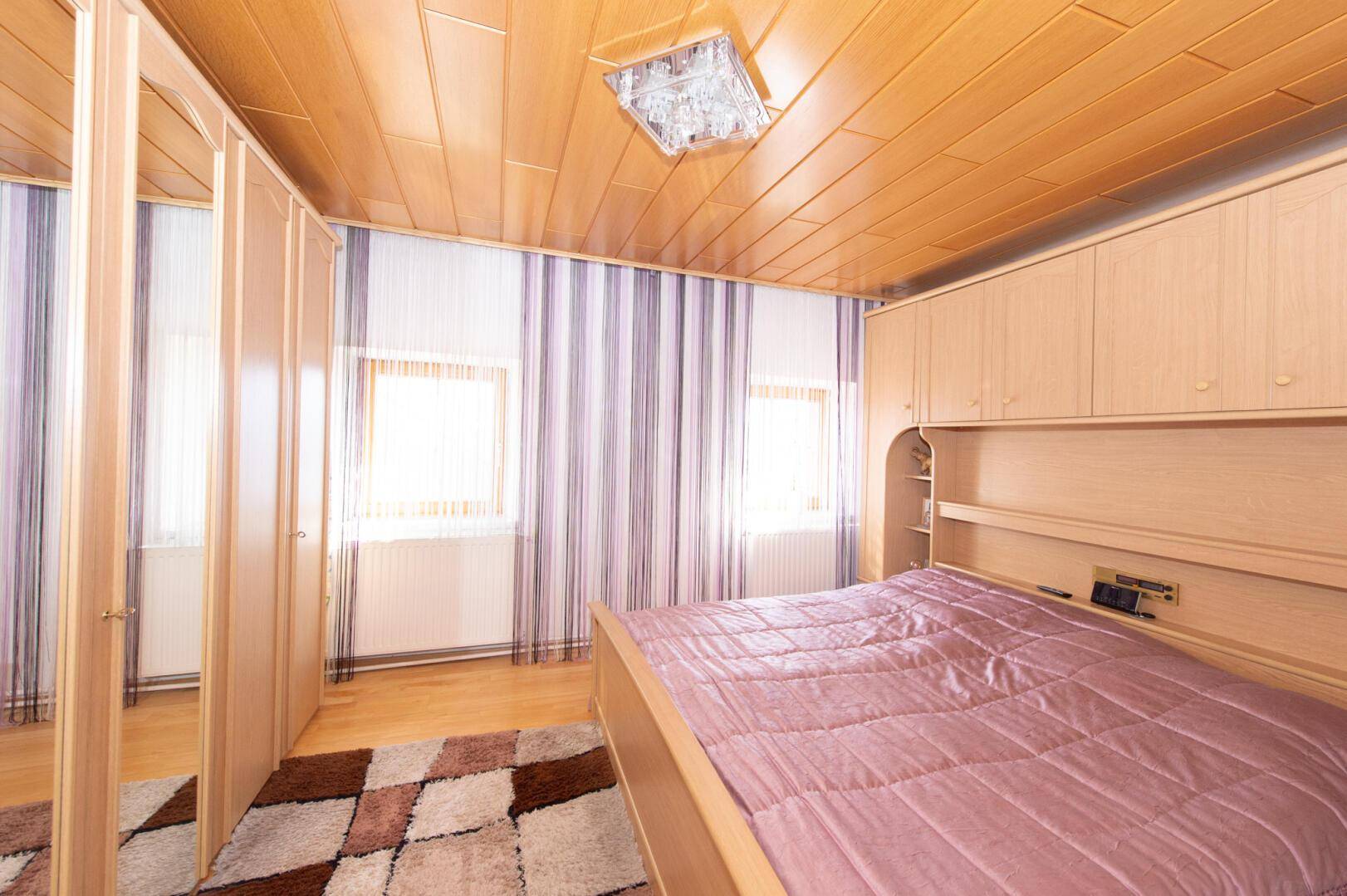Gemütliches Schlafzimmer mit Holzboden, Holzdecke und gestreiften Vorhängen.