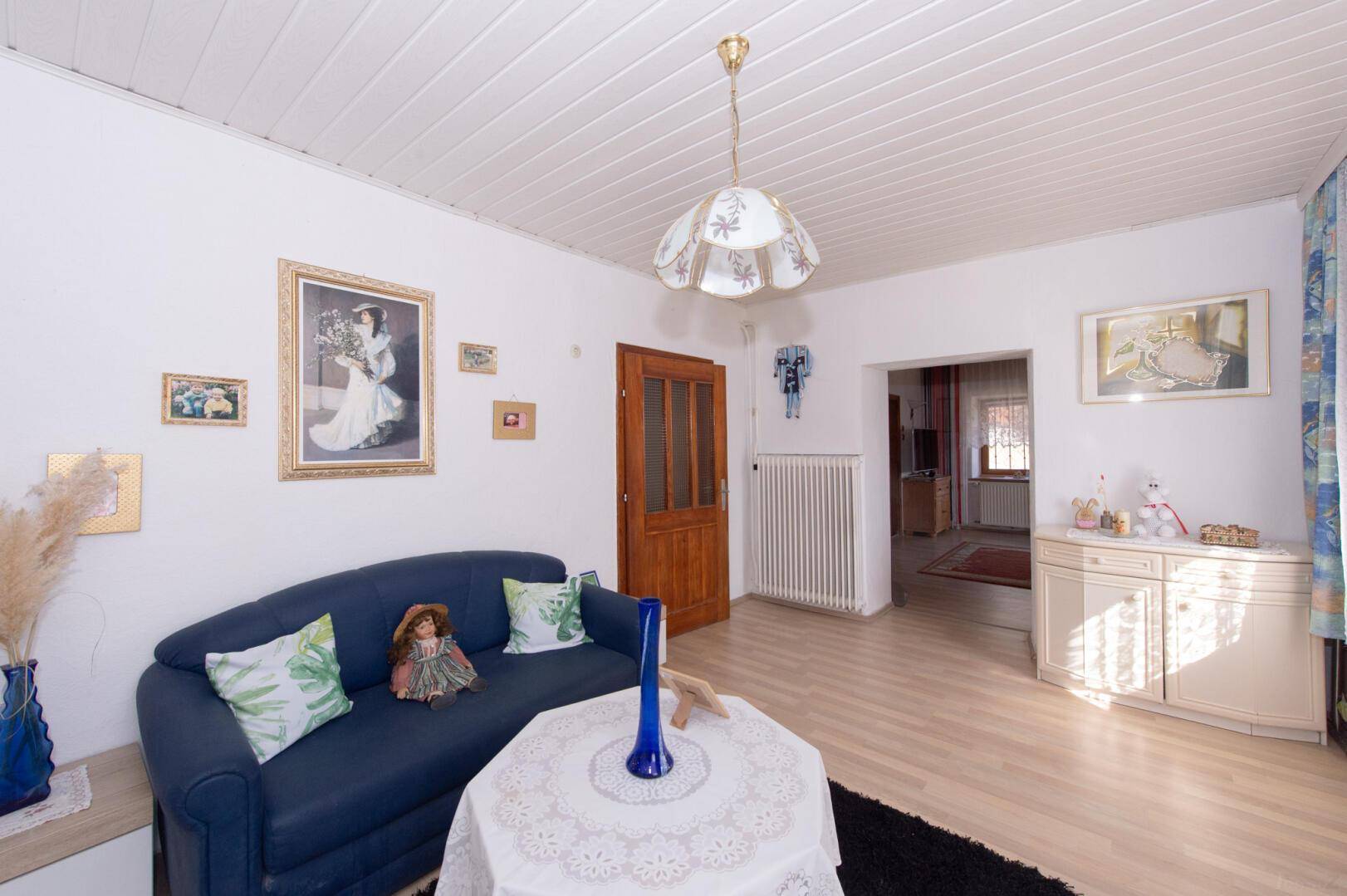 Helles Wohnzimmer mit Holzboden, blauer Couch und traditioneller Deckenverkleidung.