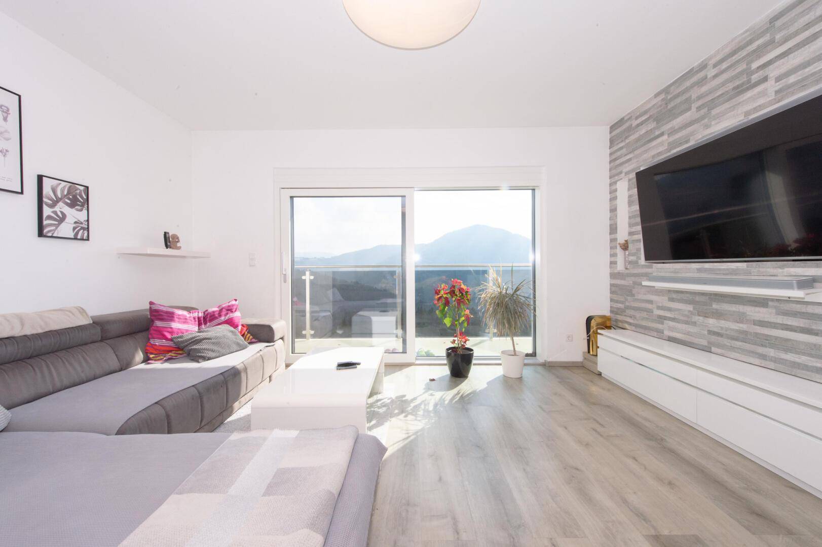 Lichtdurchflutetes Wohnzimmer mit modernem Design, Holzboden und Panoramablick auf die Berge.