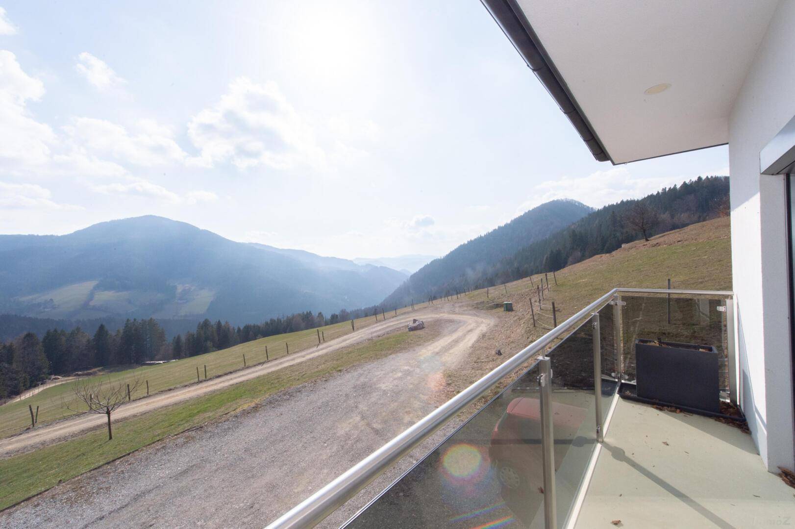 Sonniger Balkon mit Glasgeländer und weitem Blick über die umliegende Berglandschaft.