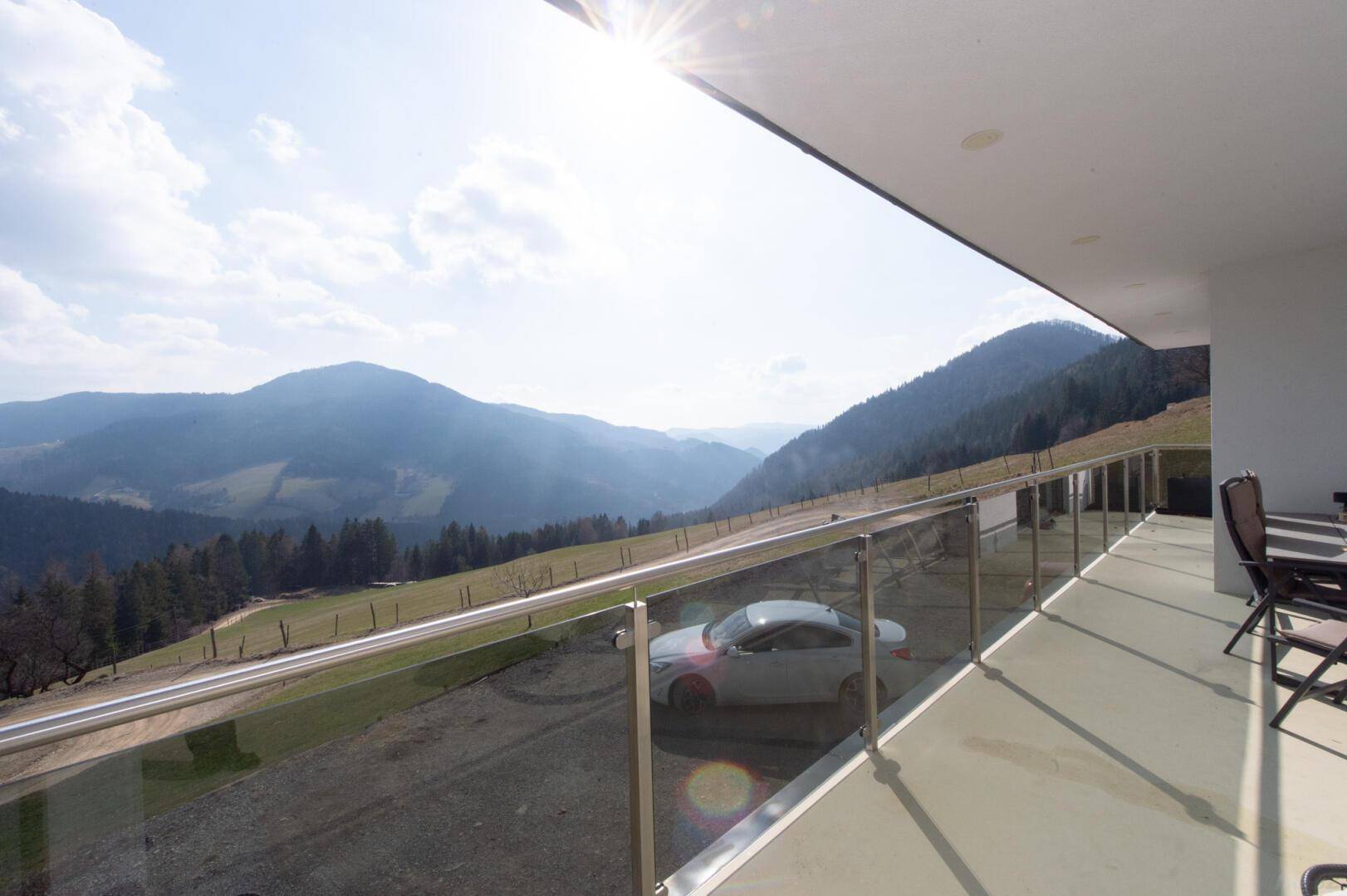 Geräumiger Balkon mit Glasbrüstung, Sitzgelegenheiten und beeindruckendem Bergblick.