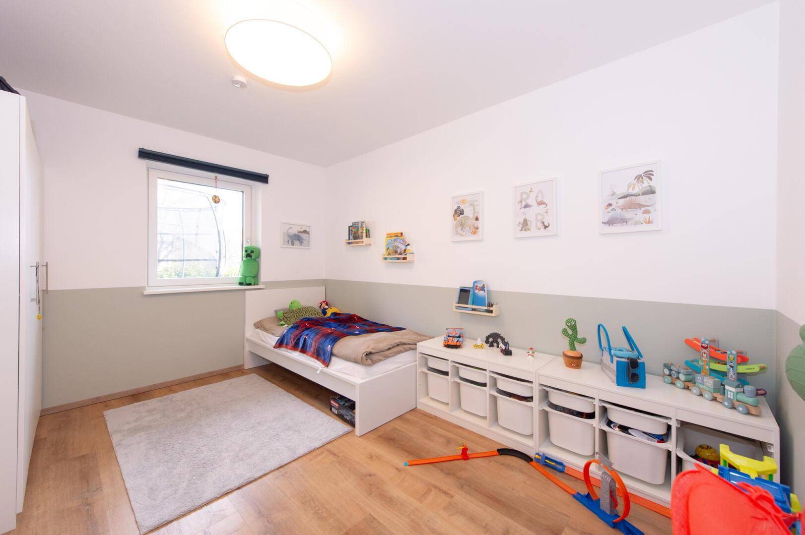 Freundliches Kinderzimmer mit Holzboden, Spielzeug und hellem Fenster.