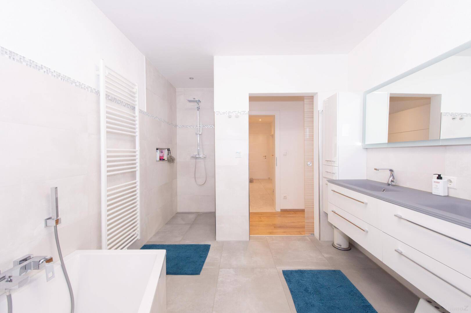 Helles Badezimmer mit Badewanne, Dusche und beheiztem Handtuchhalter.