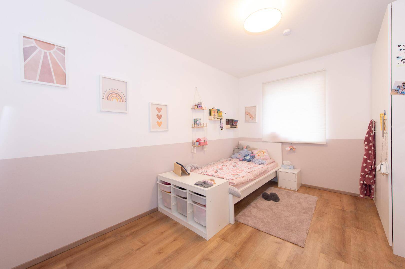 Kinderzimmer mit hellem Holzboden, modernem Bett und verspielter Dekoration.