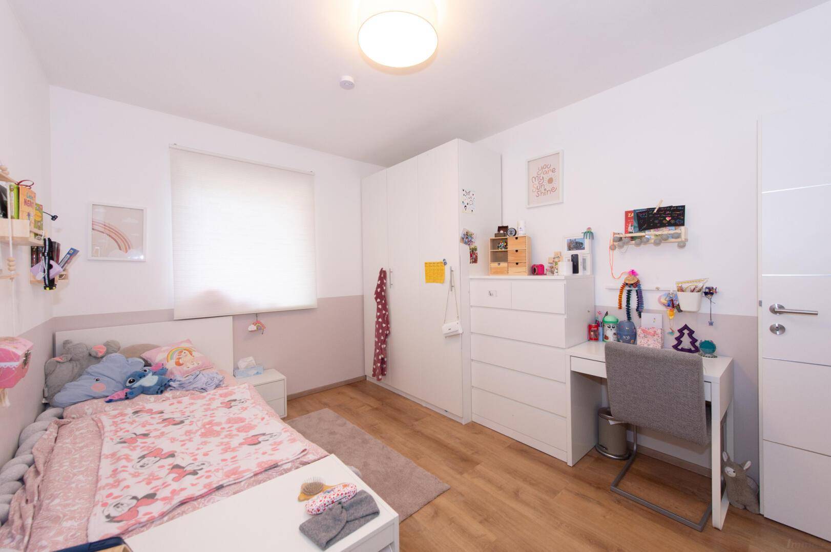 Helles Kinderzimmer mit Schreibtisch, Kleiderschrank und freundlicher Gestaltung.