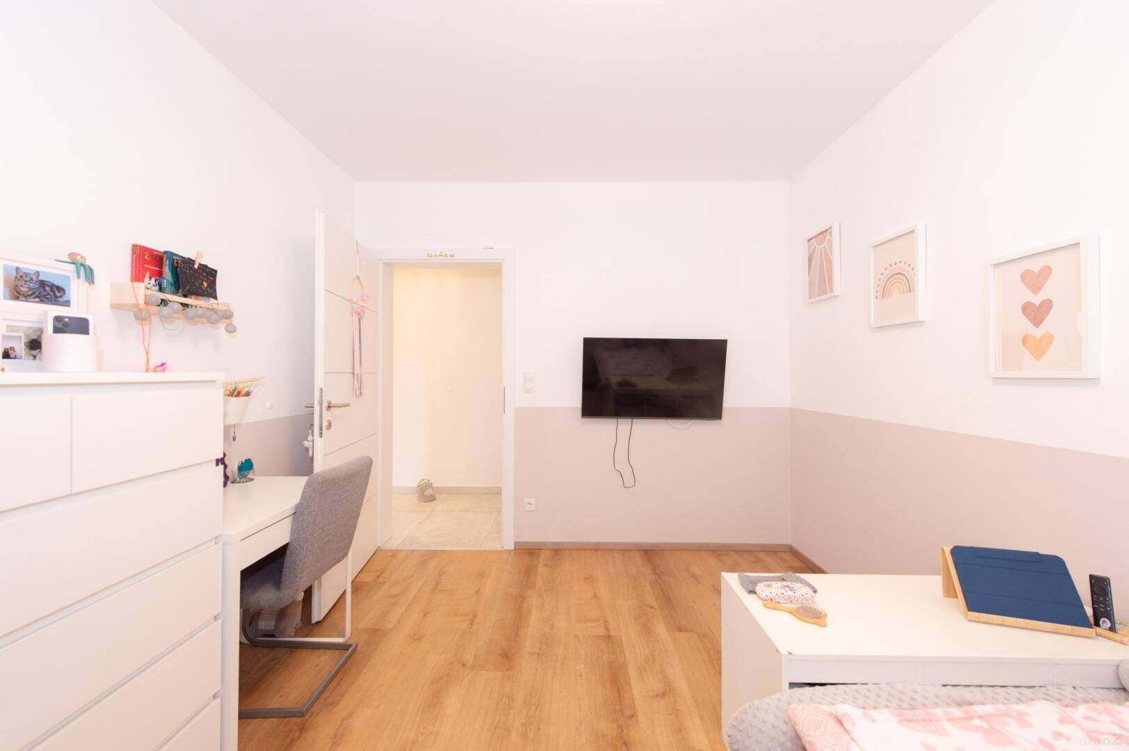 Kinderzimmer mit Holzboden, Wandfernseher und Zugang zu einem weiteren Raum.
