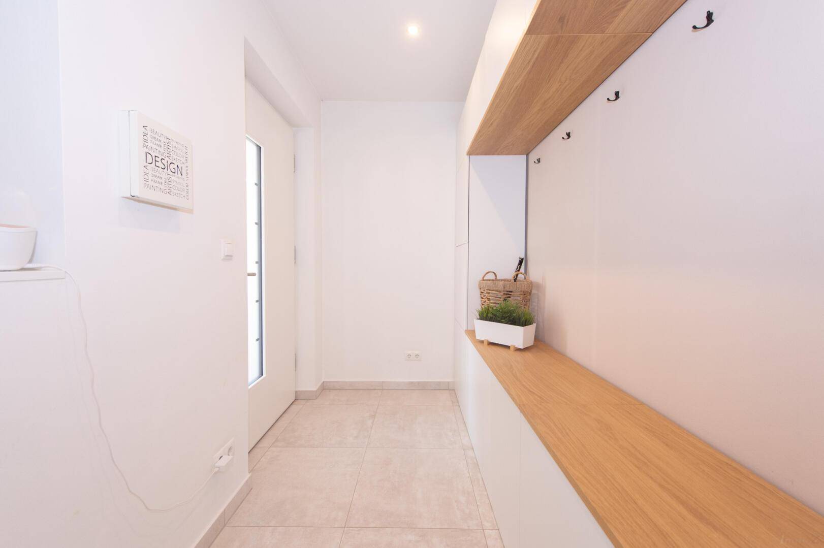 Heller Eingangsbereich mit Fliesenboden und integrierter Garderobe aus Holz.