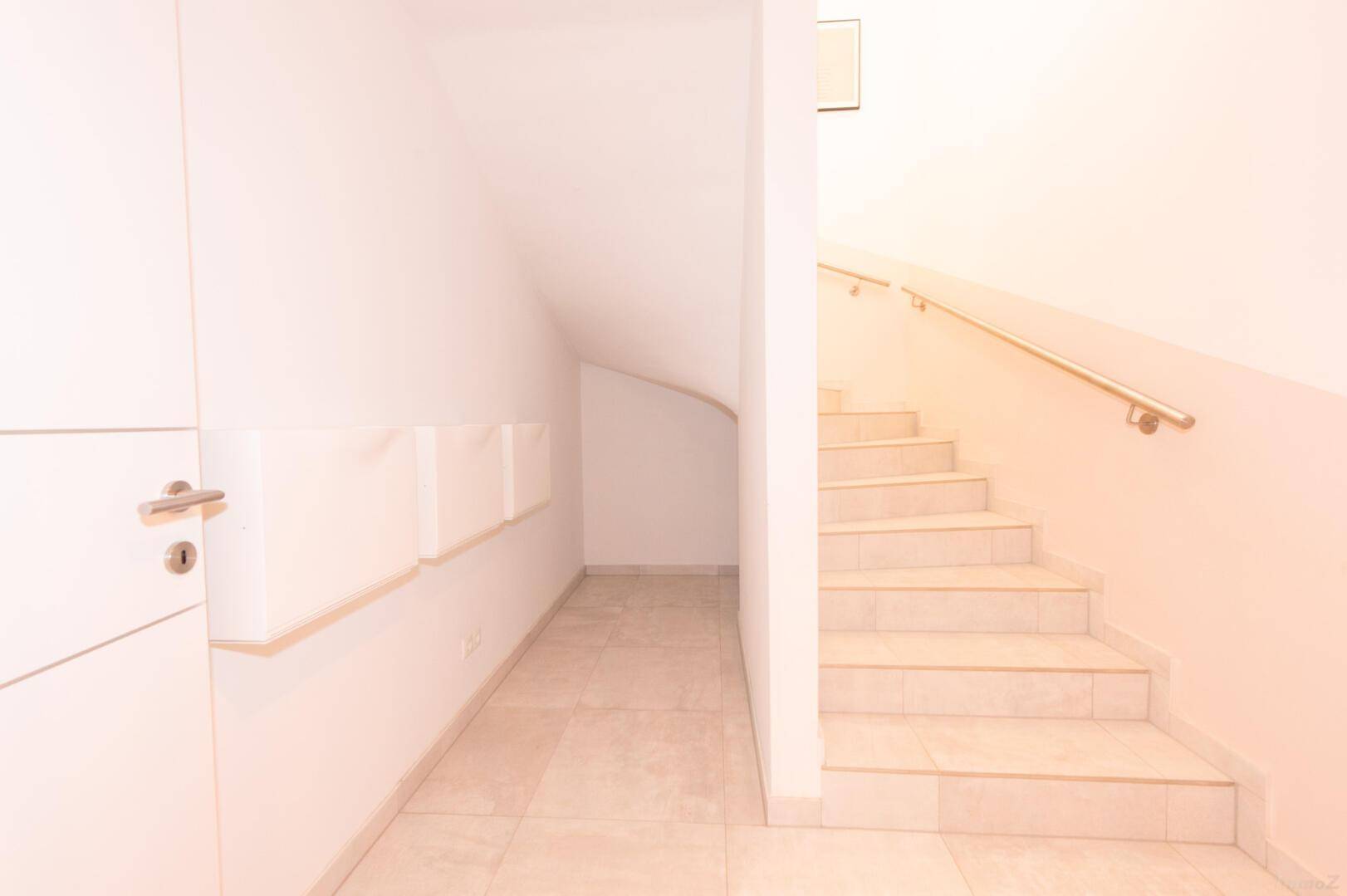 Heller Flur mit Fliesenboden und praktischem Stauraum unter der Treppe.