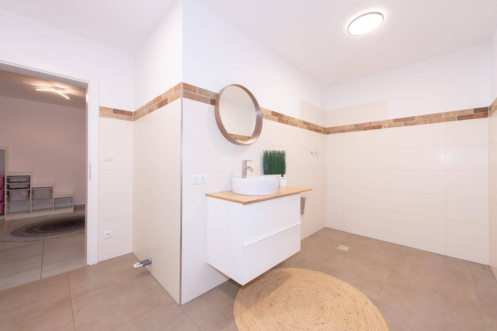 Helles Badezimmer mit modernem Waschbecken, runden Spiegel und Fliesenboden.
