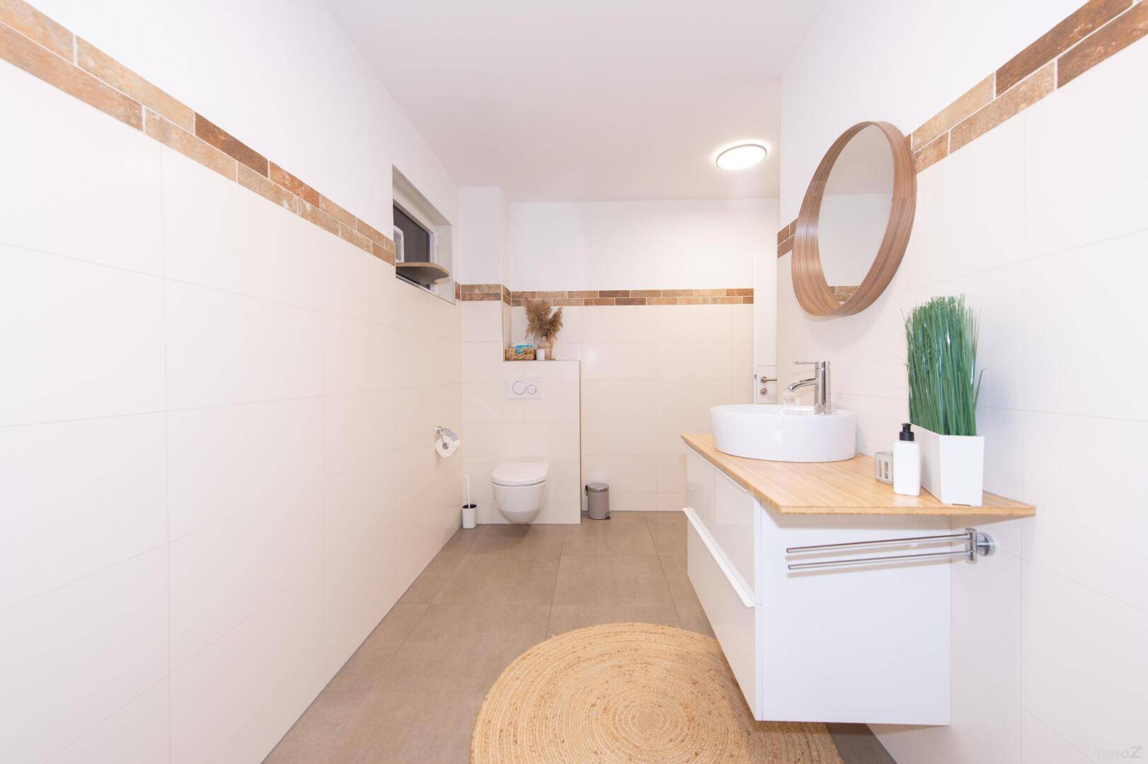 Modernes Badezimmer mit rundem Spiegel, Aufsatzwaschbecken und hellen Fliesen.