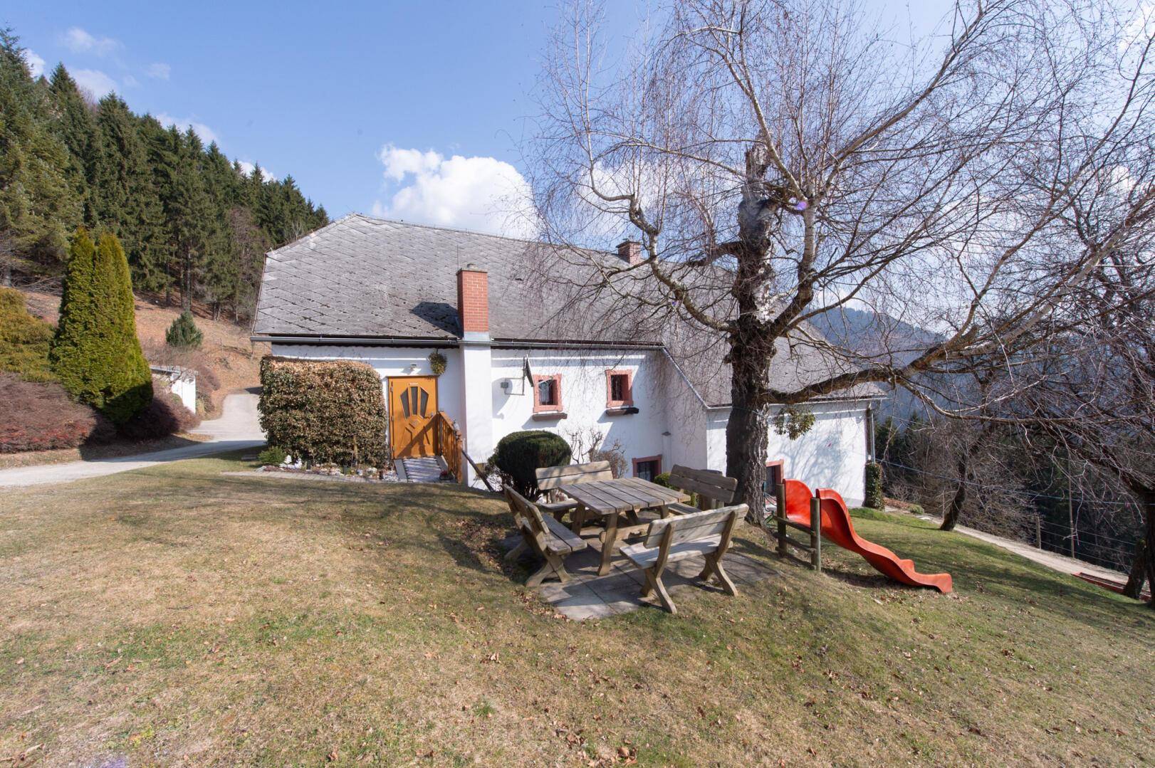 Gartenbereich des traditionellen Hauses mit Holztisch, Bänken und Kinderrutsche.