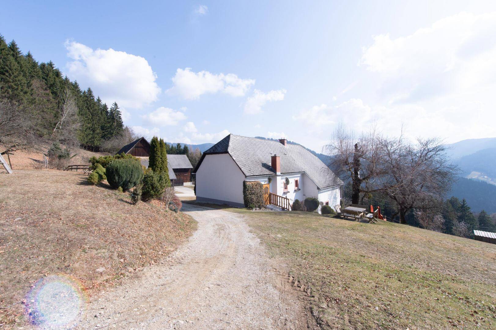 Traditionelles Bauernhaus in ländlicher Umgebung mit Schotterweg und Bäumen.
