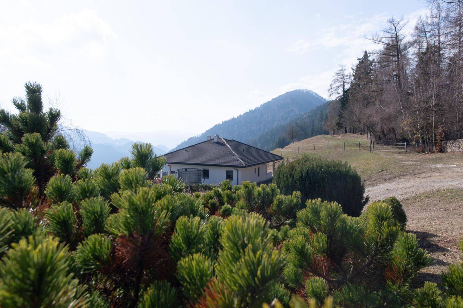 Modernes Haus in ländlicher Umgebung, umgeben von grünen Büschen und Bergen.