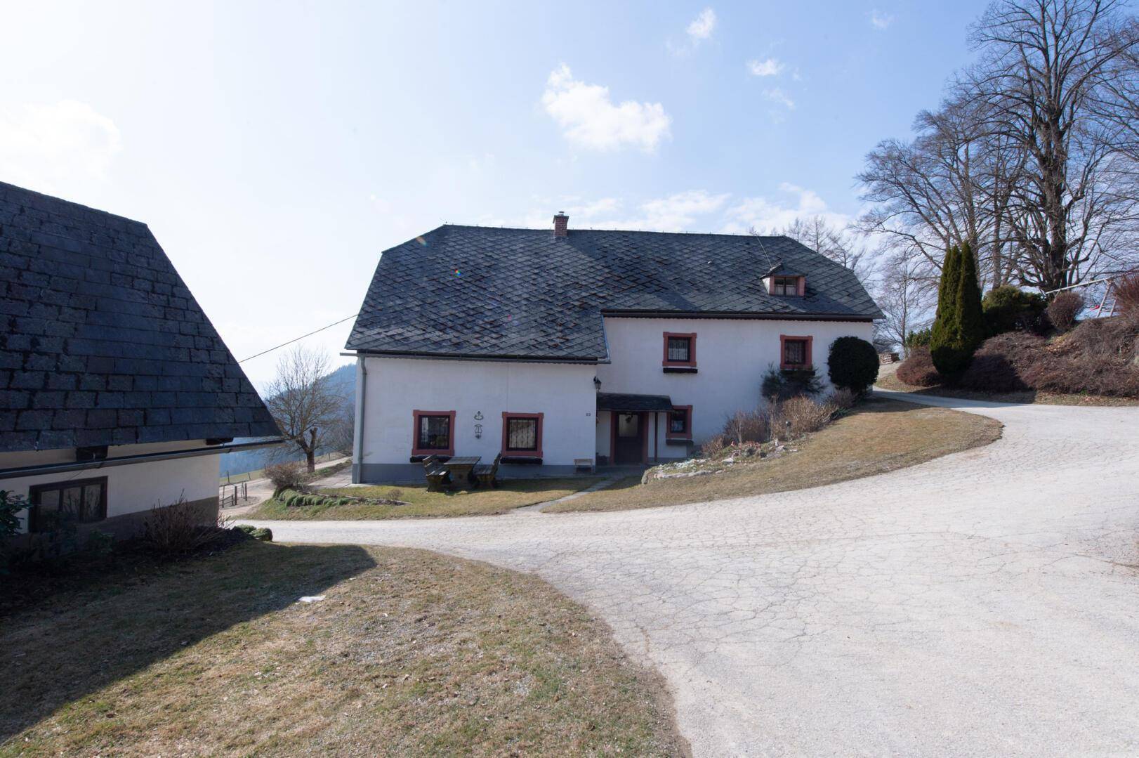 Weißes, traditionelles Haus mit rotem Fensterrahmen und Satteldach in ländlicher Lage.